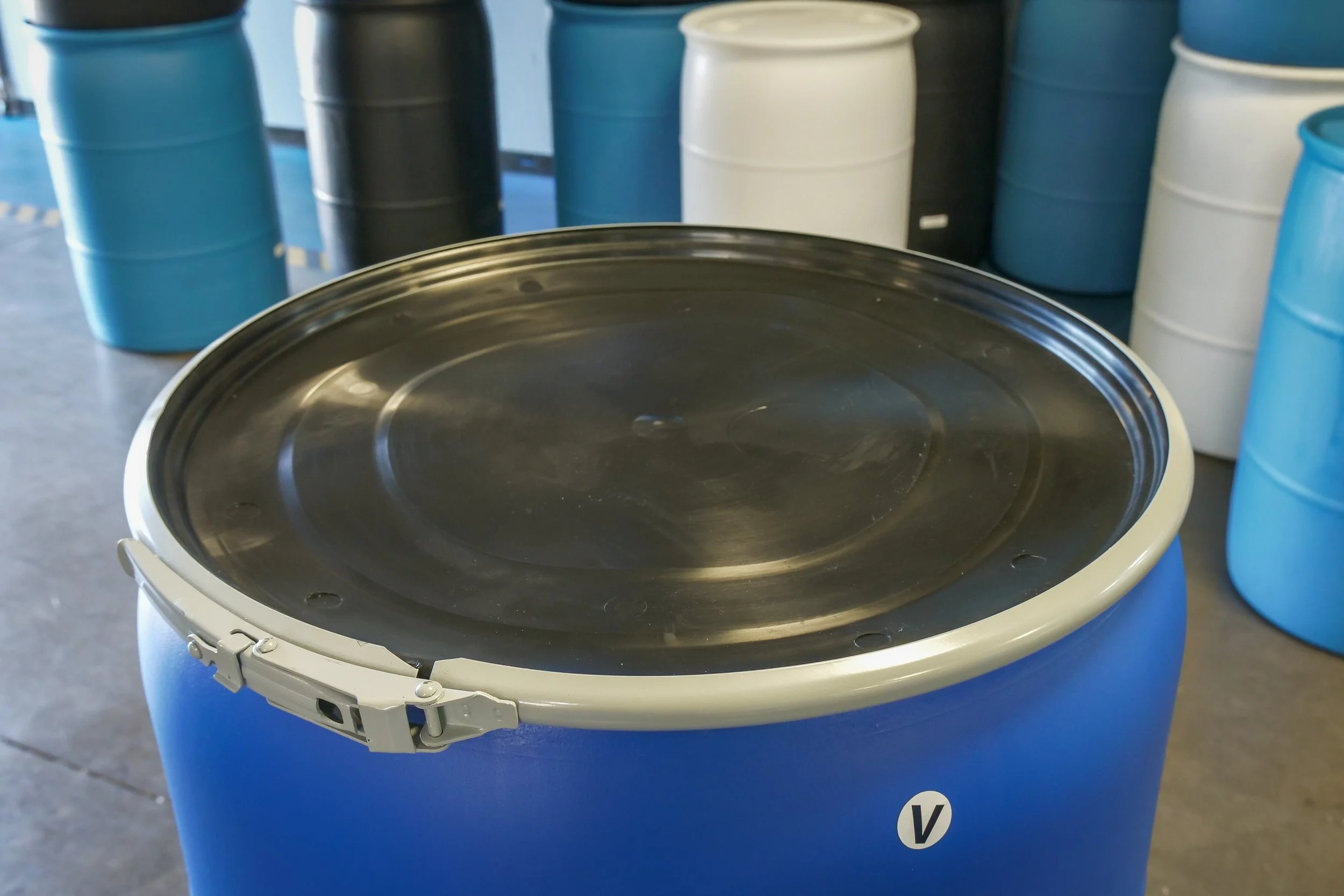 Blue industrial drum with a closed lid in an industrial setting, with similar drums in the background.