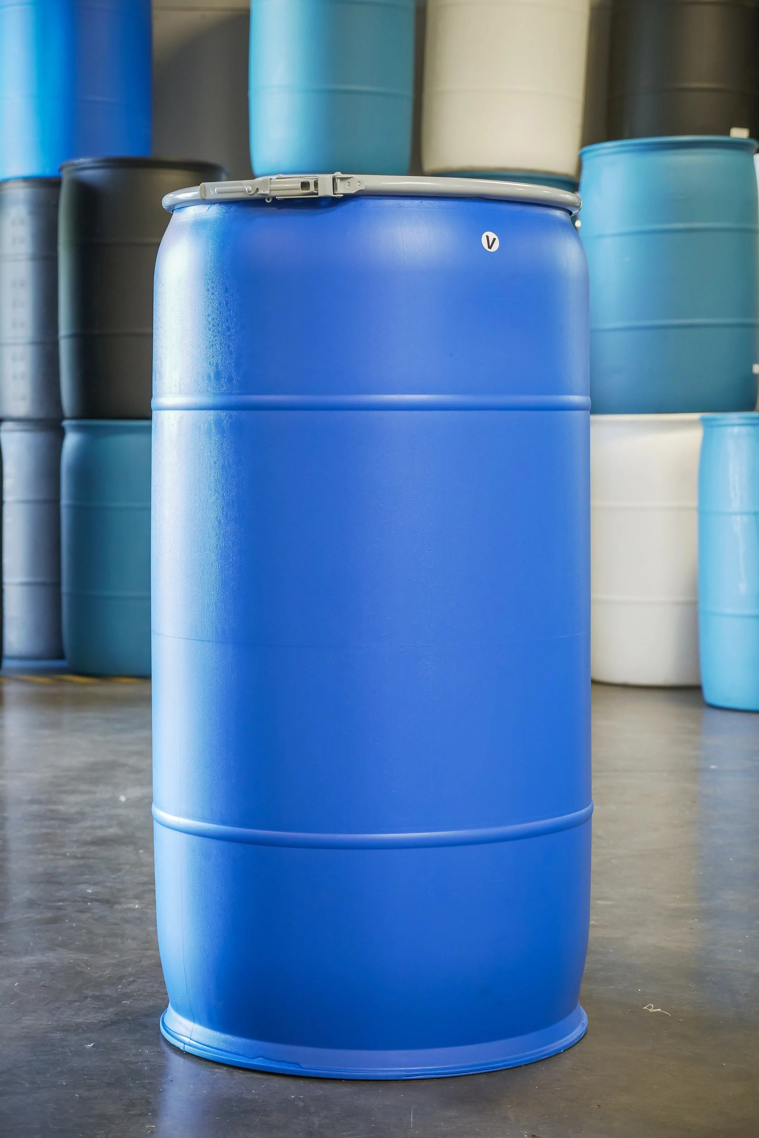 Blue plastic barrel in warehouse with stacks of various colored barrels in the background.