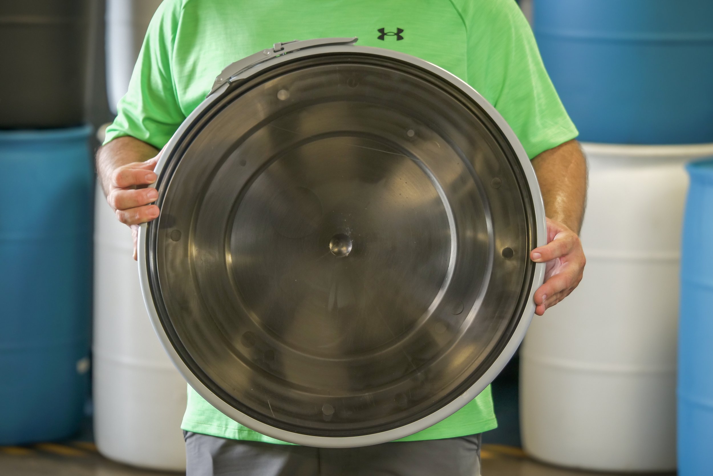 Person holding a large stainless steel washing machine drum in a laundry setting.