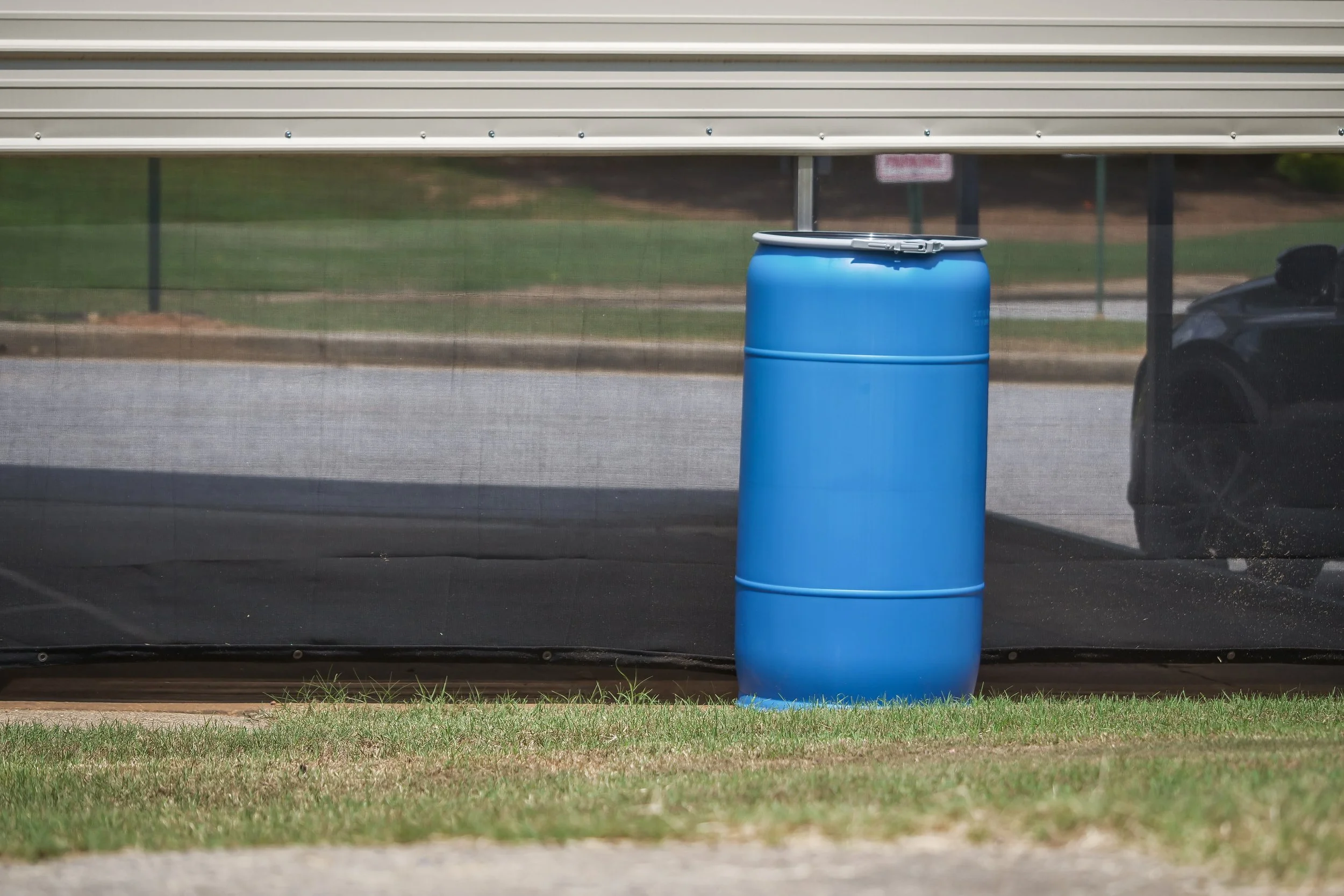 A blue plastic barrel behind a metal and roller shutter garage door with a black car partially visible on the right side.