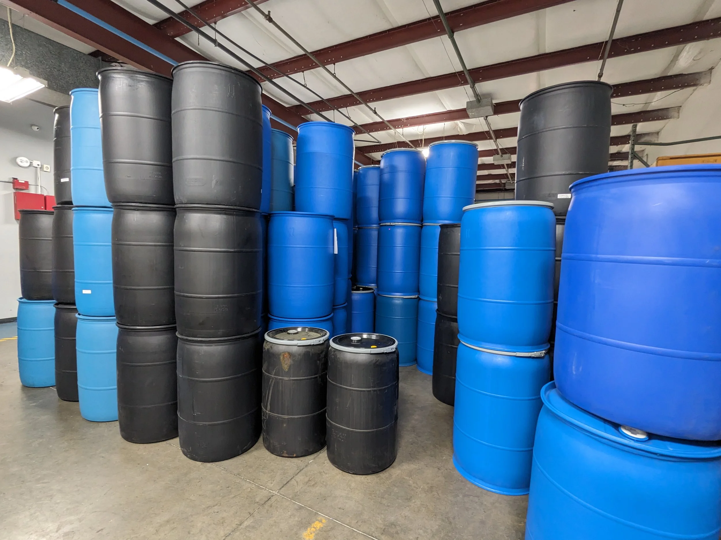 Stacked black and blue industrial barrels in a warehouse.