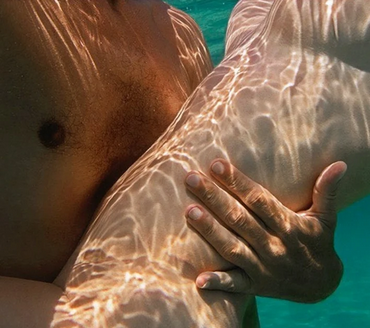 man with dark skin, holding nude woman with pale skin underwater.