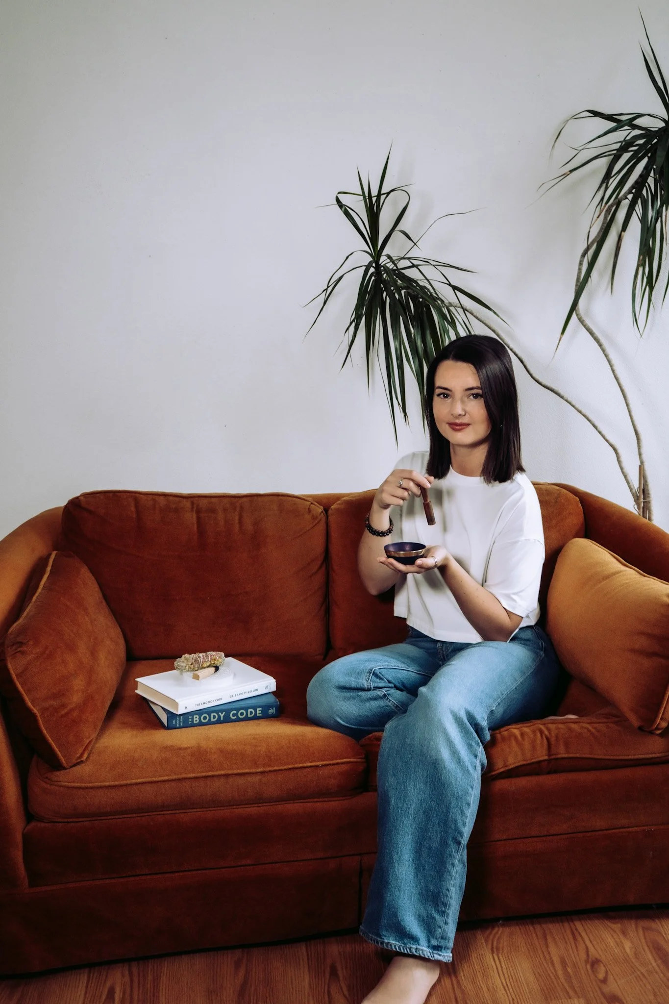 Energy healing practitioner Dennim Daniels of Greenlight Healing in Baraboo, Wisconsin, specializes in Emotion Code and Body Code sessions. A girl with dark hair and a white shirt sitting on the couch. Calming and grounding energy.