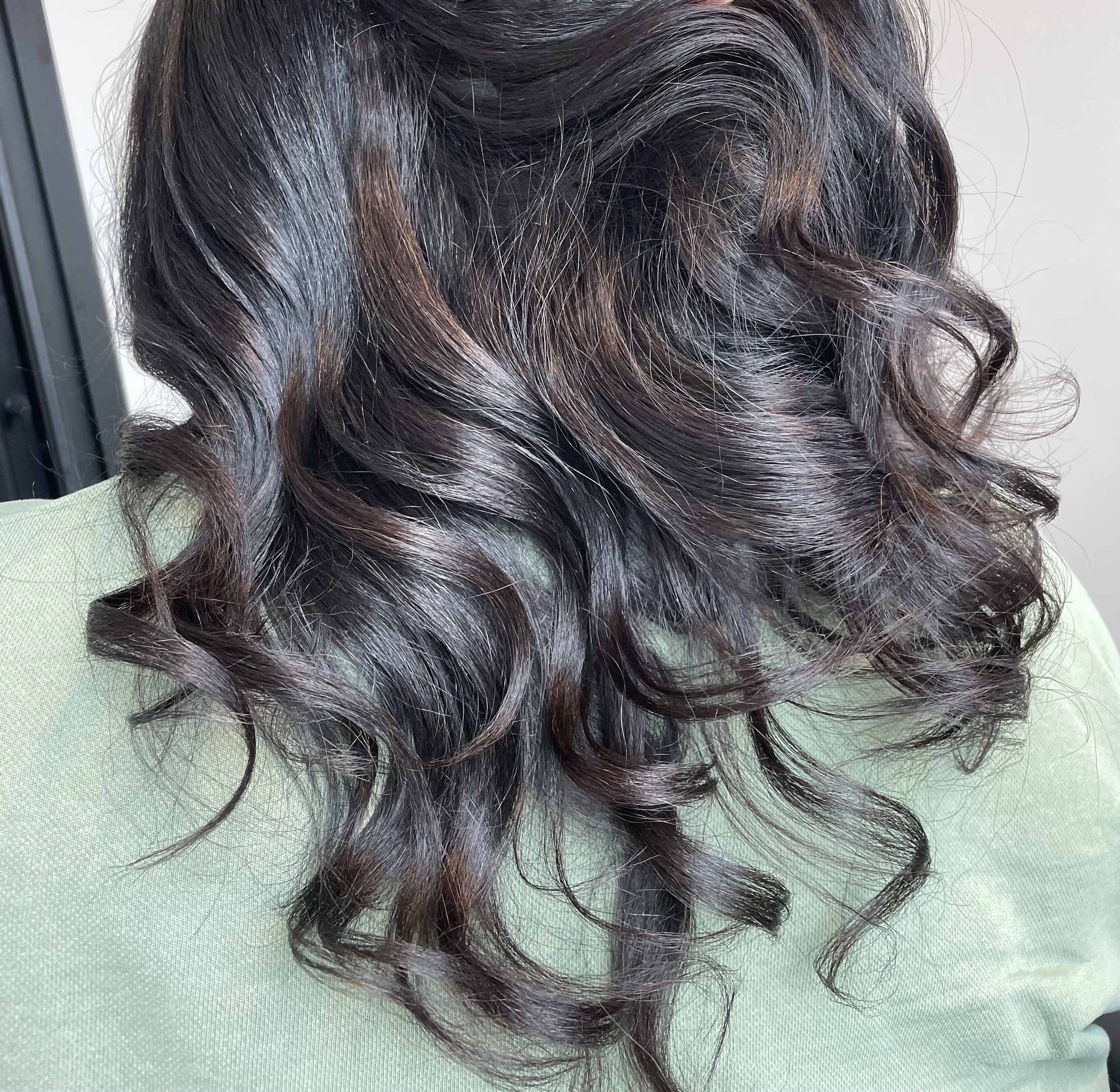 Back of a person's head with shoulder-length, wavy, dark brown hair with subtle reddish highlights.