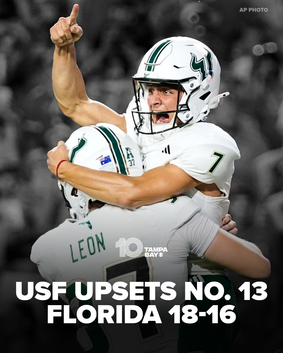 Group of football players in white uniforms celebrating a victory, one player with a number 7 helmet is being embraced by teammates, background blurred.