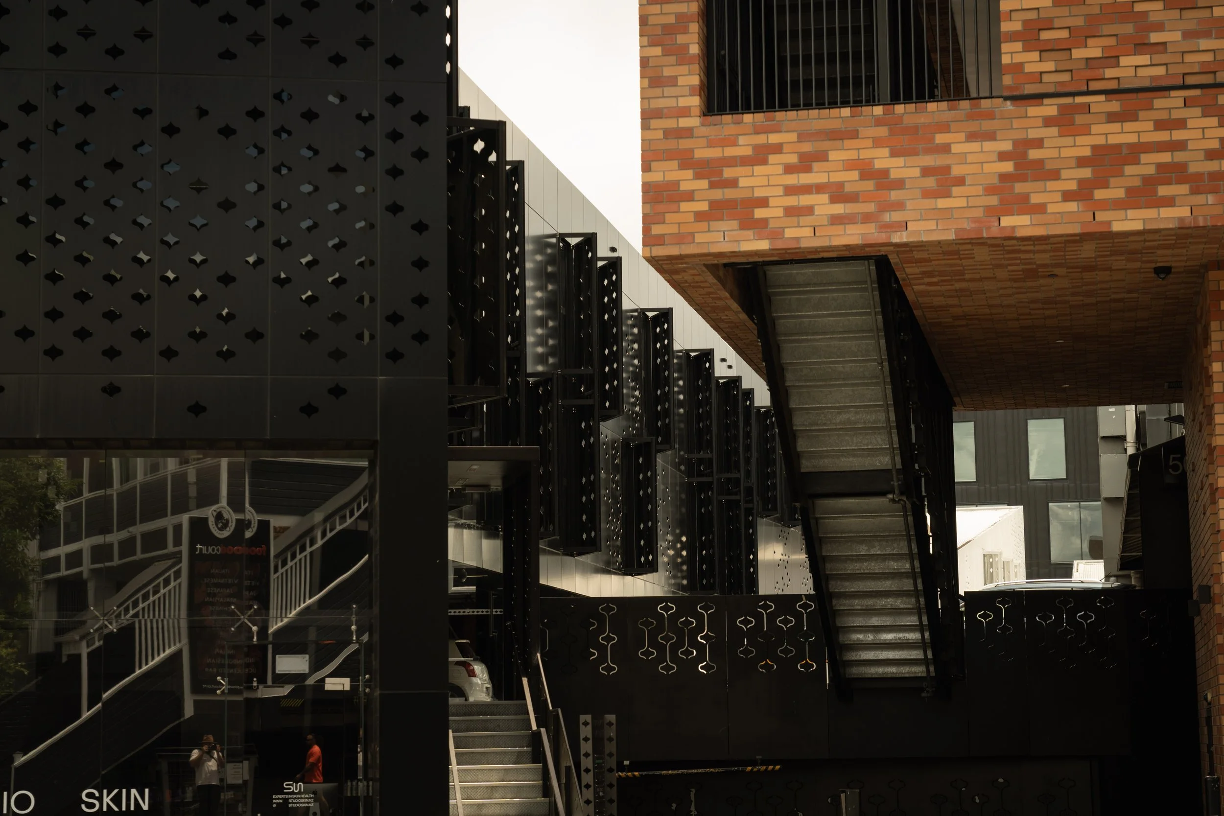 Modern building with black perforated panels, metal staircase, and brick upper level.