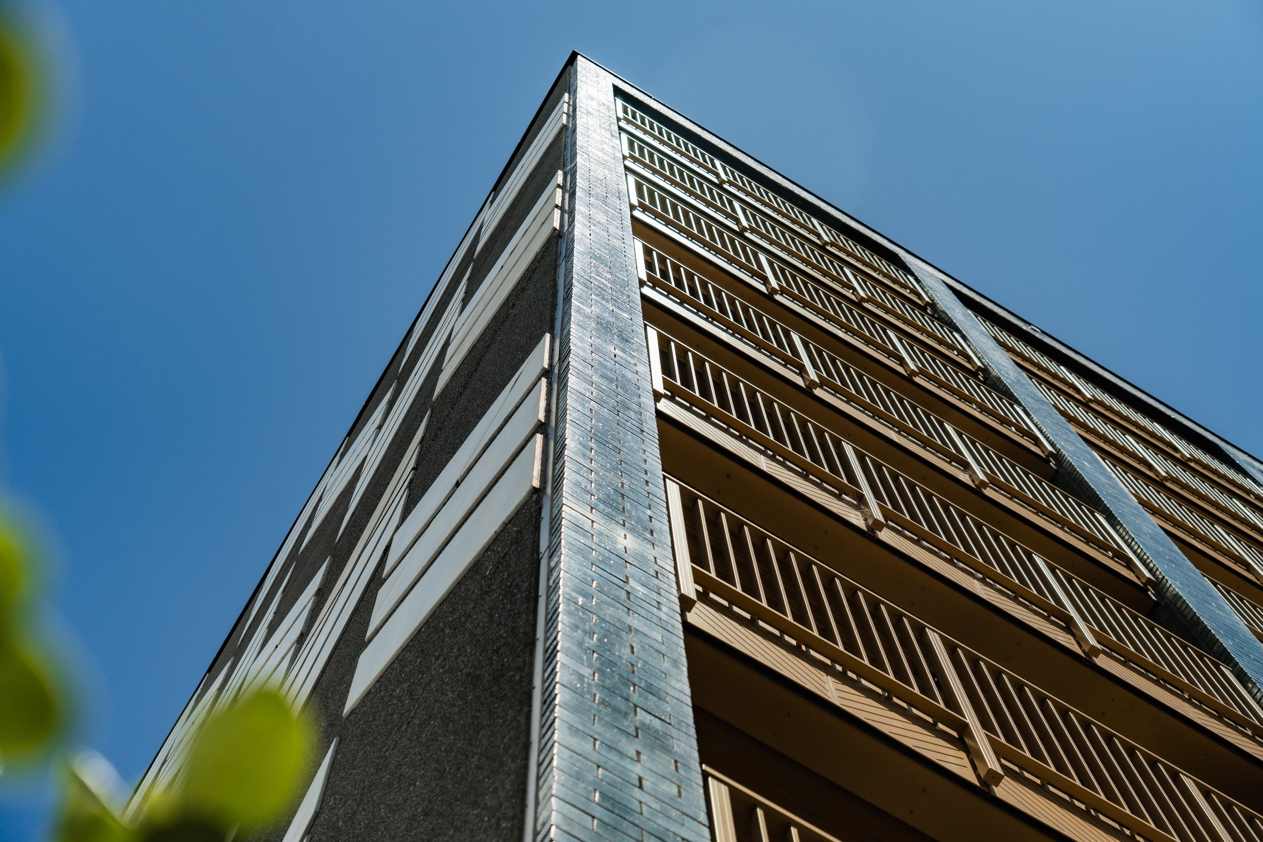Low-angle view of a modern multi-story building with balconies and a corner set against a clear blue sky.
