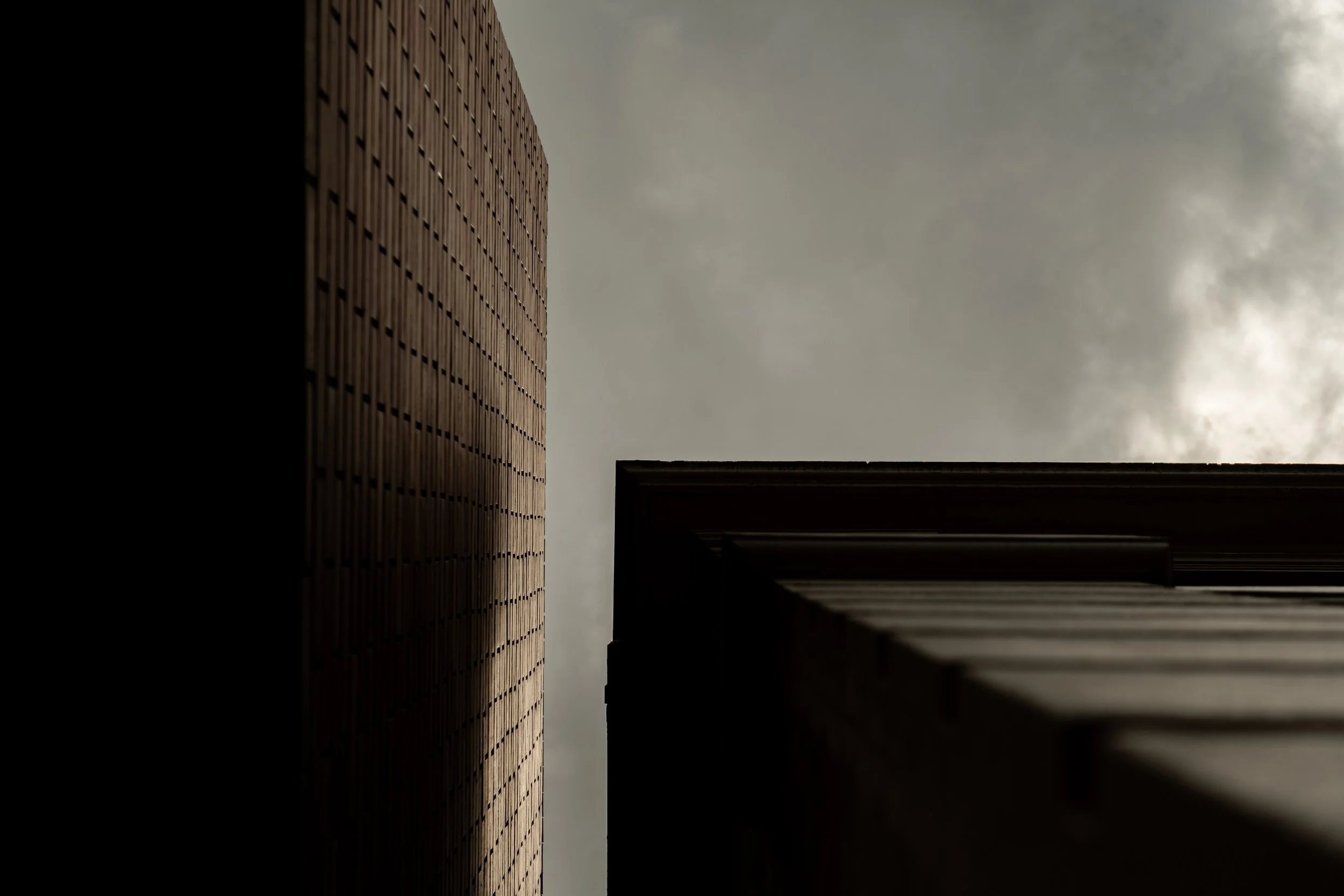 Upward view of two modern buildings with dark cloudy sky in the background.