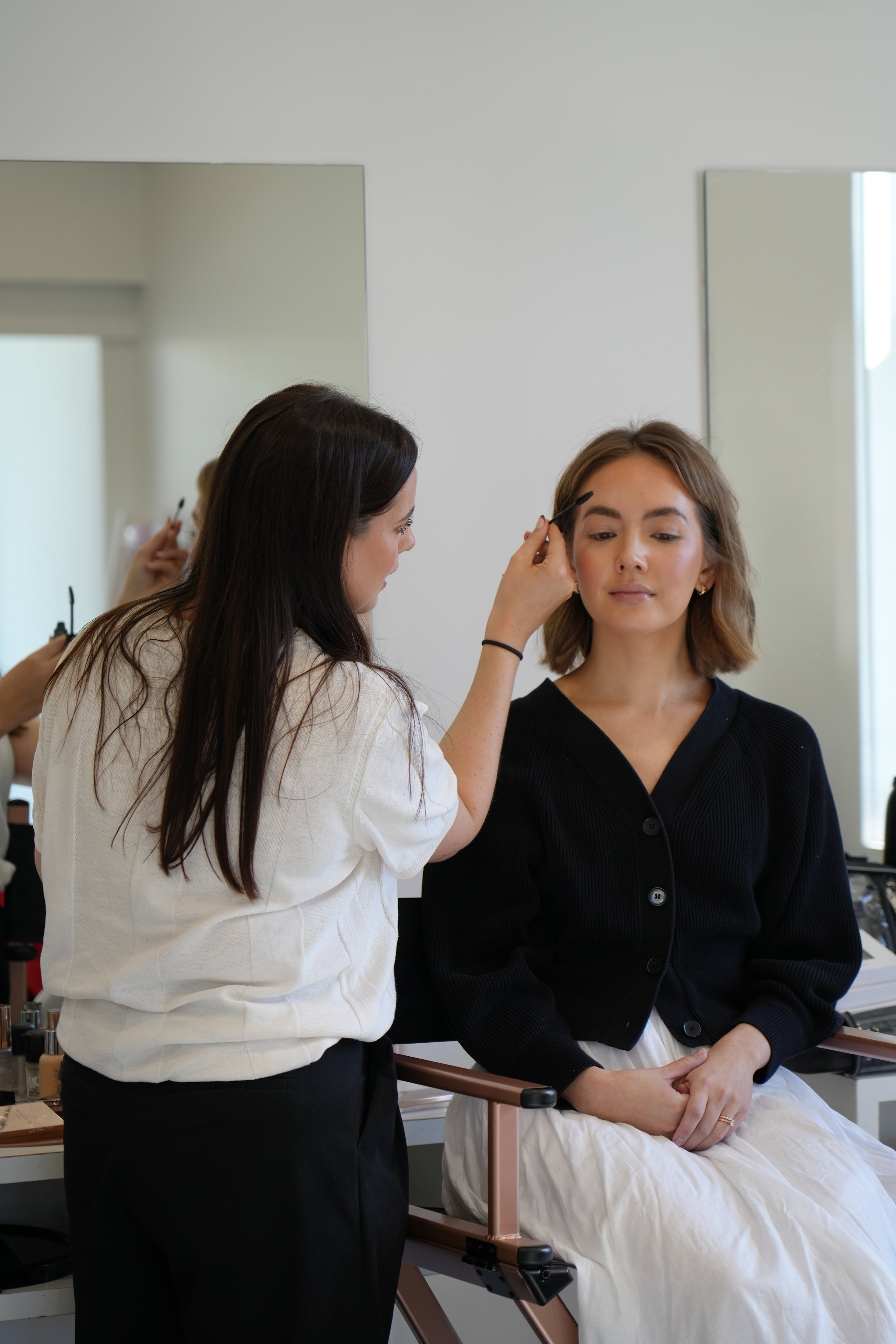 Makeup artist applying makeup to a woman seated in a salon or makeup studio.