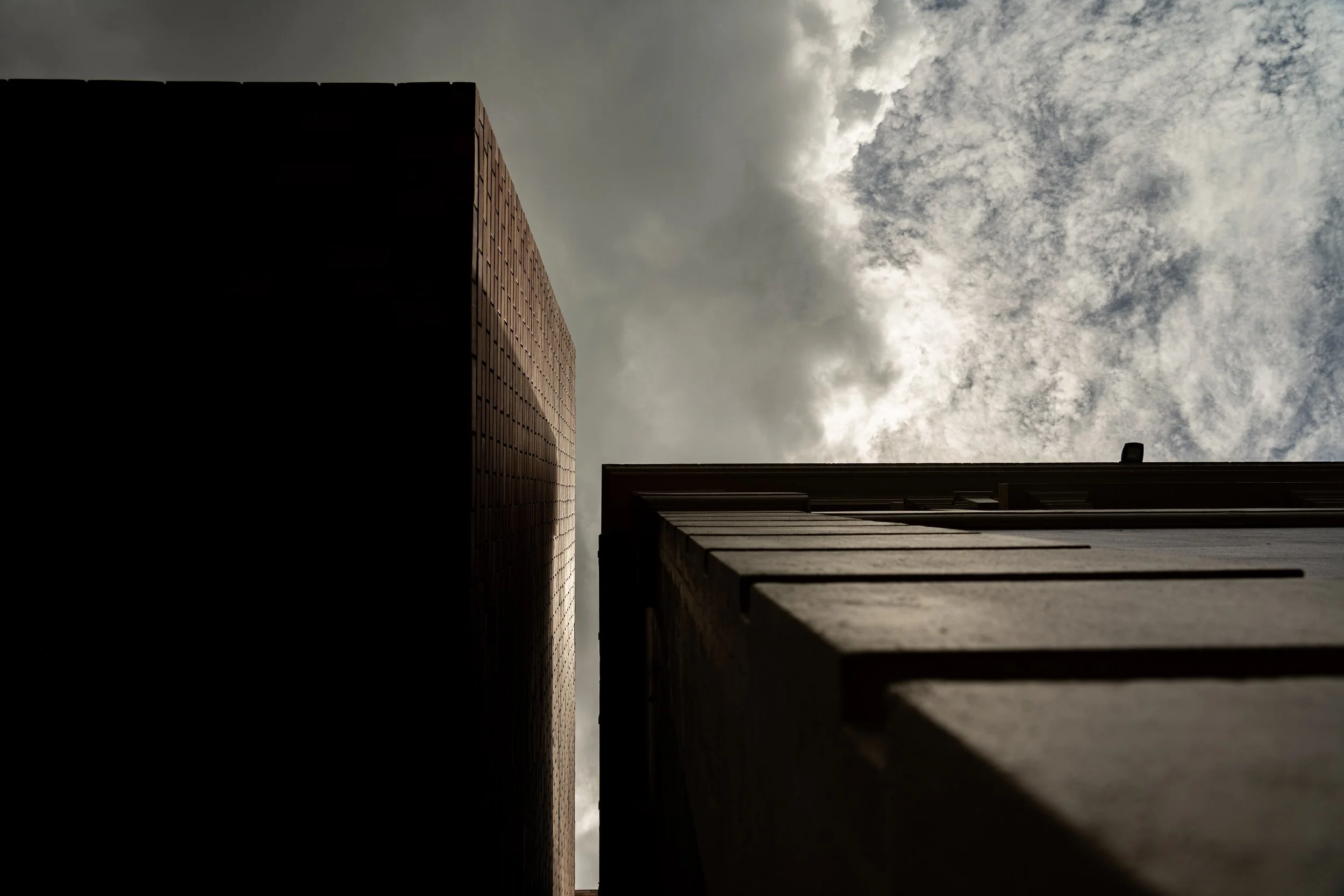Looking up between two tall buildings toward a cloudy sky.