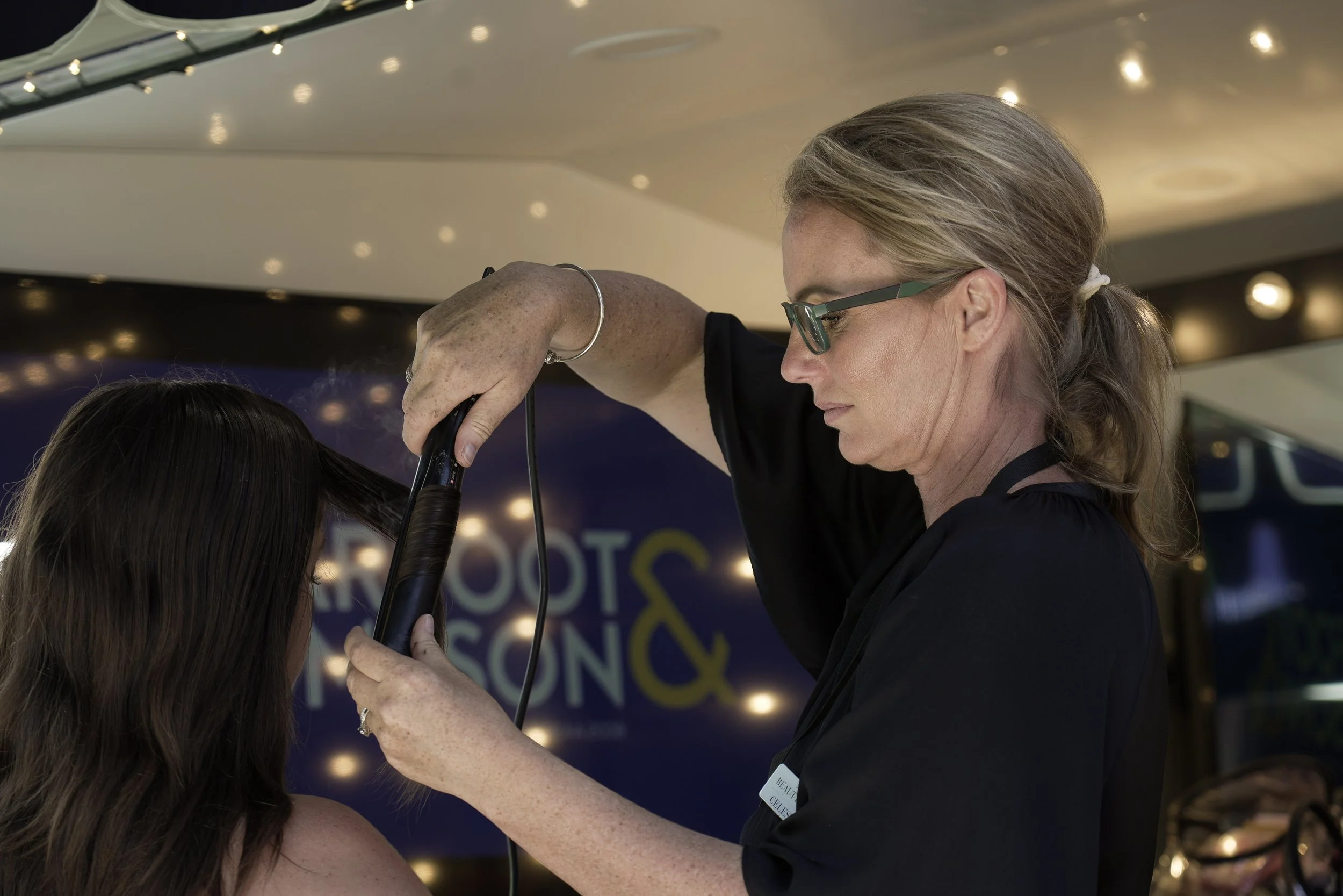 A hairstylist using a flat iron to straighten a woman's hair inside a salon.