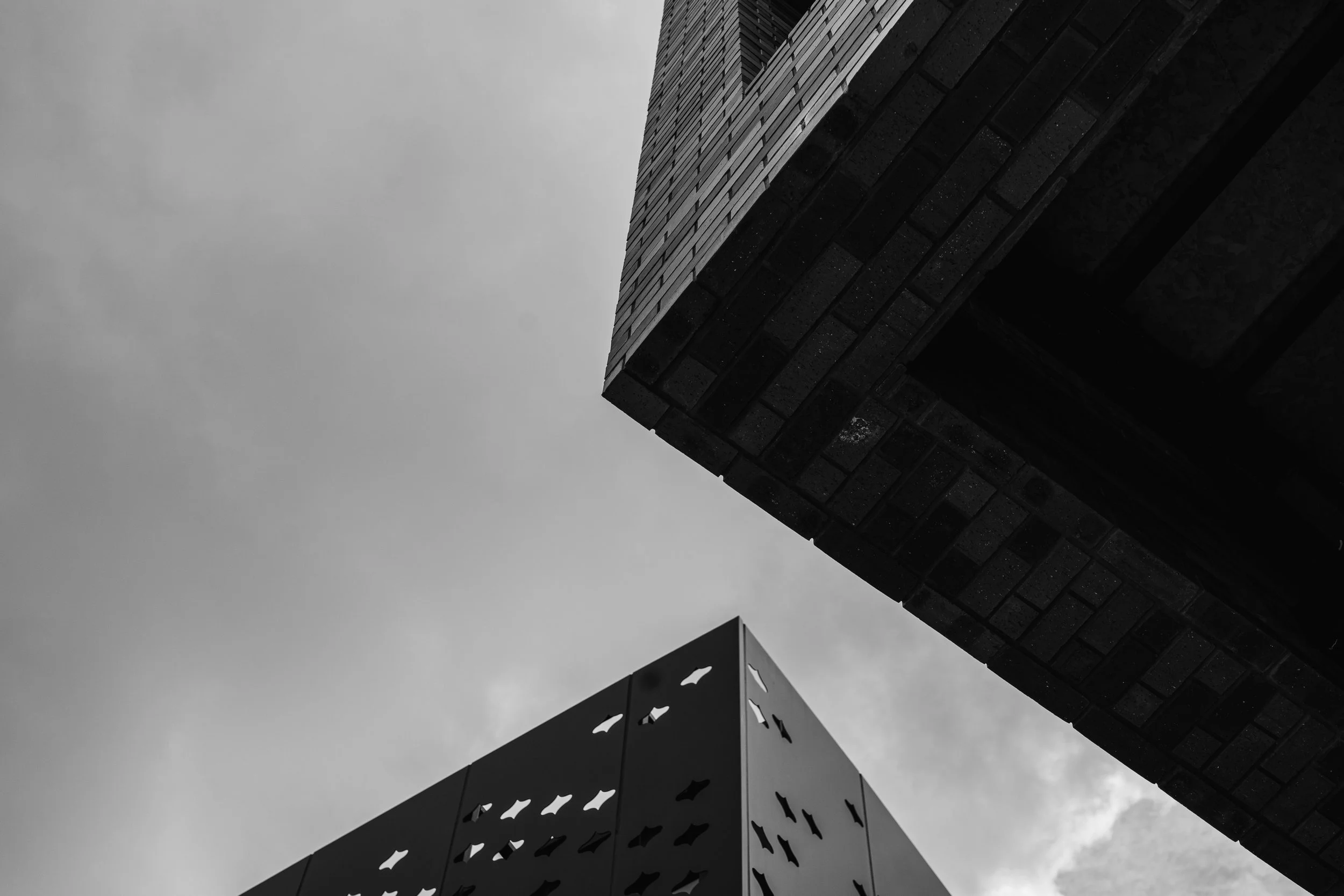 Black and white photo of two modern buildings viewed from below, with a cloudy sky in the background.