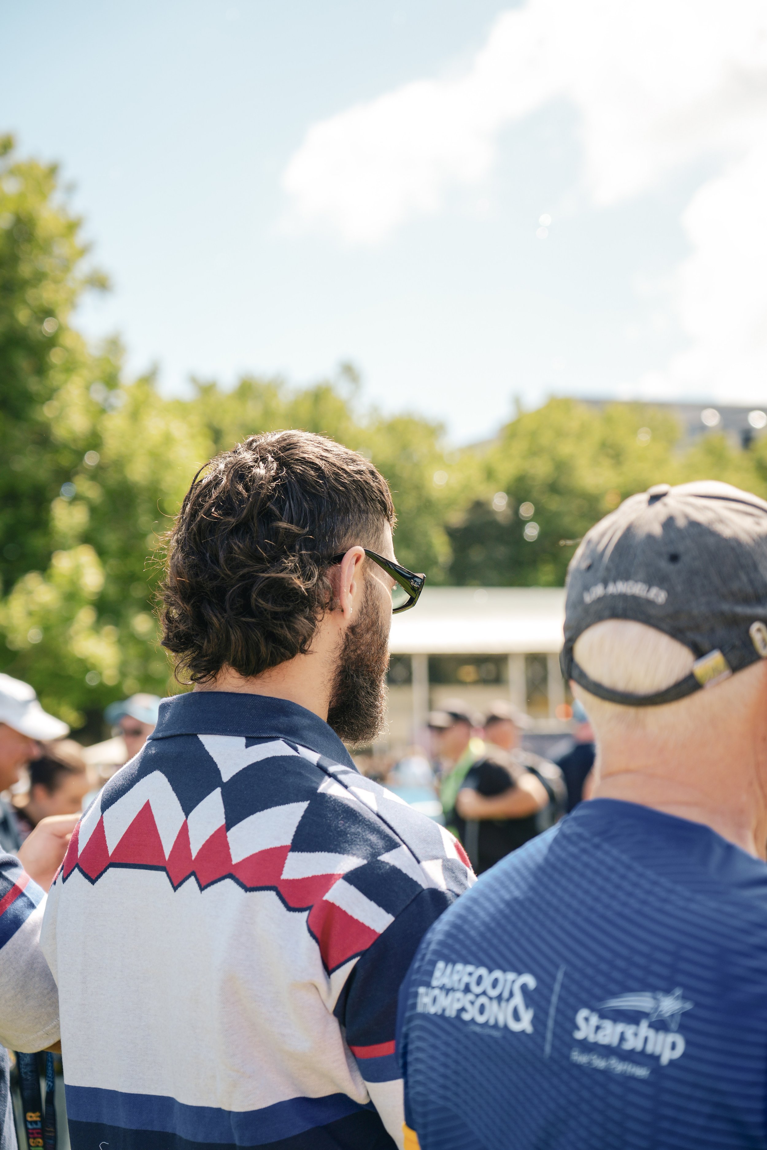 People outdoors at a gathering, with a background of trees and a partly cloudy sky.