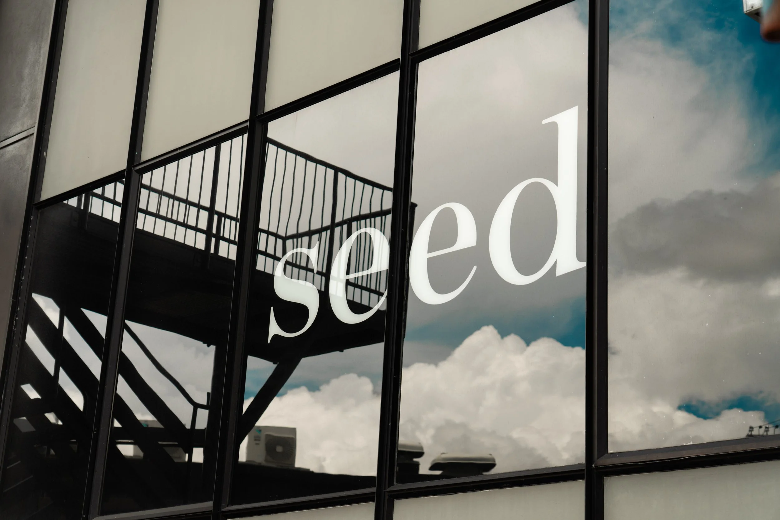 Reflection of clouds and a staircase on a glass window with the word 'seed' written on it.