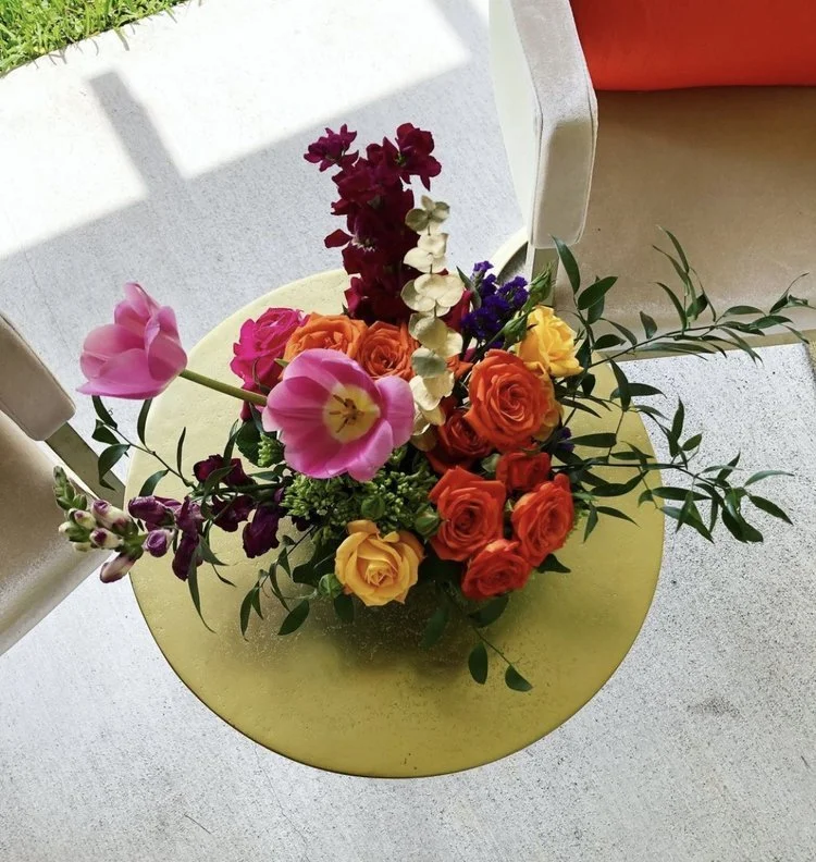 Colorful mixed flower bouquet with pink, orange, yellow, purple, and white flowers on a yellow table.