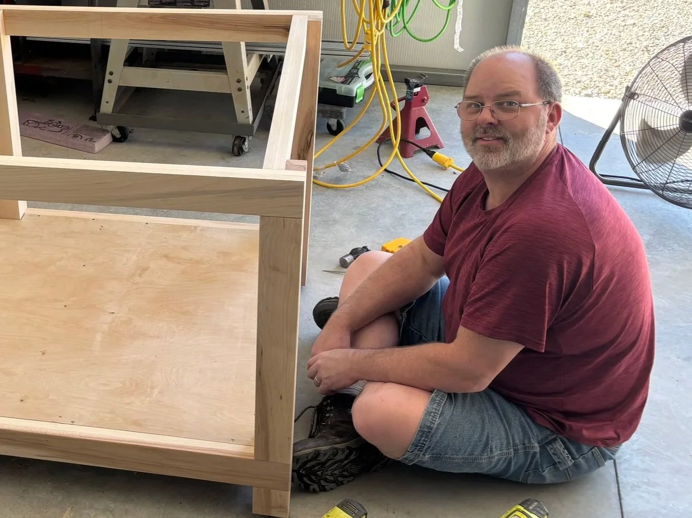 Bryan Clark sitting on the floor of his shop working on a wood table.