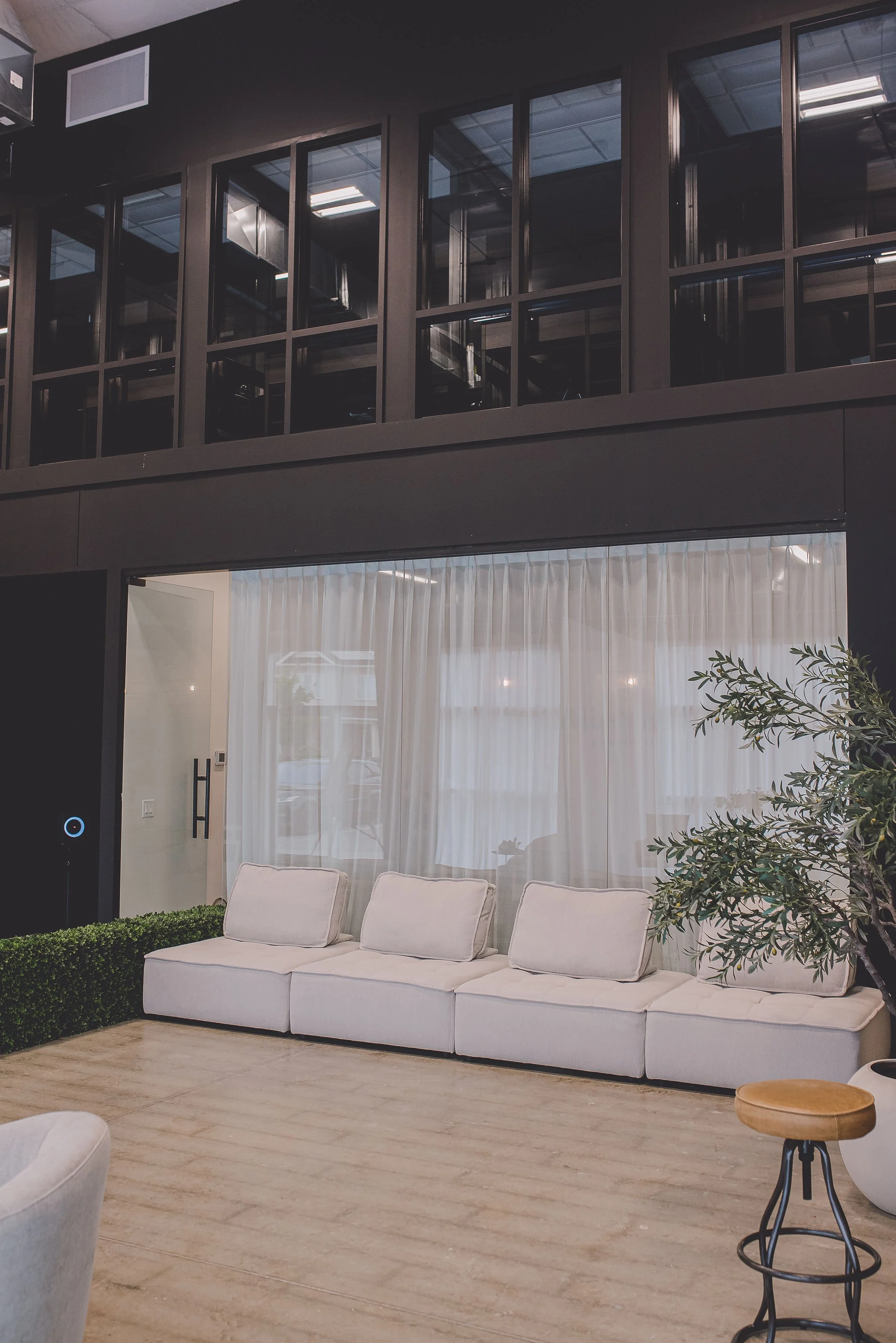 Modern indoor lounge area with white sofa, sheer curtains, potted plant, and minimalist decor.