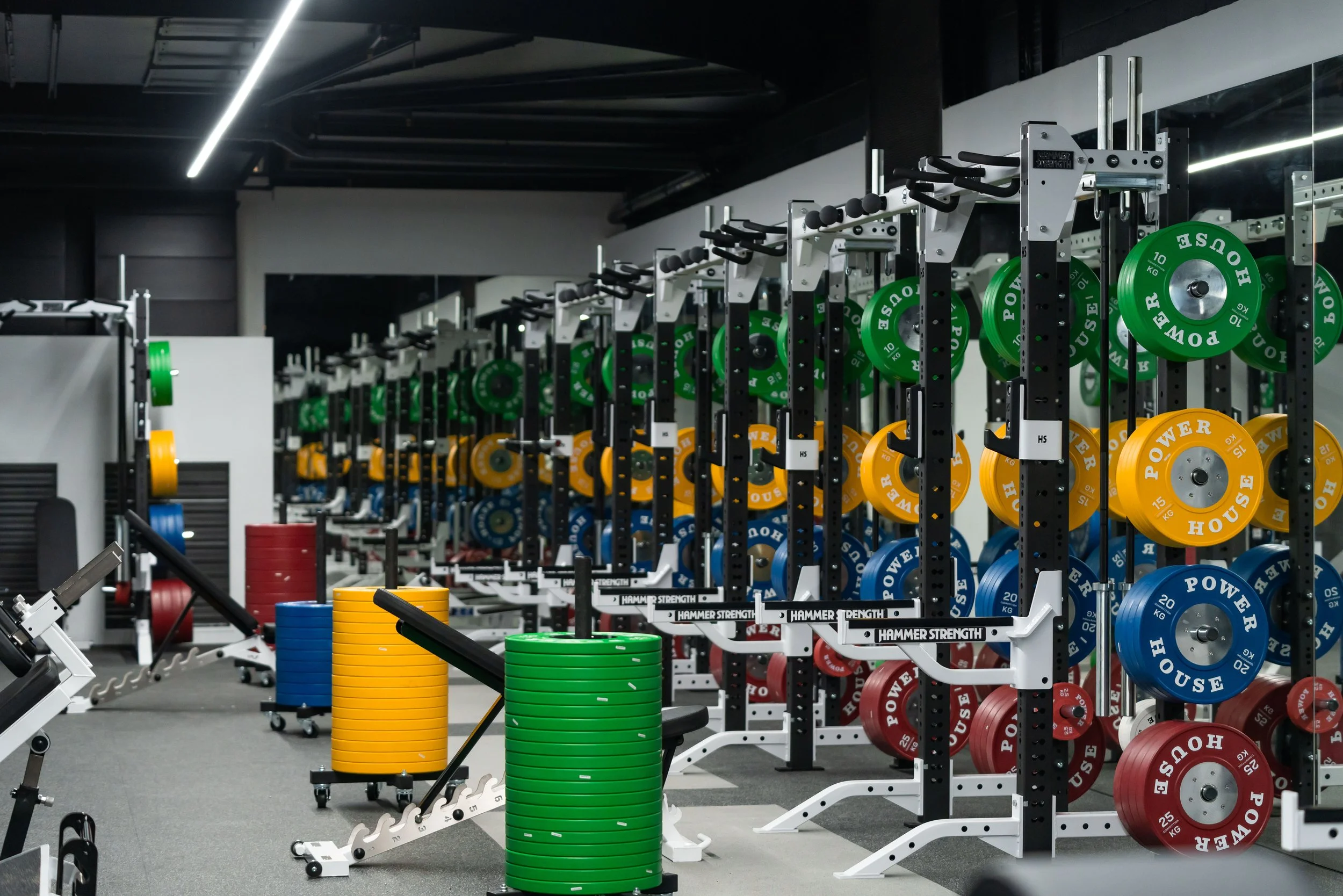 A gym with weightlifting equipment, including rows of weight plates in green, yellow, blue, and red, stored on racks, and exercise machines.