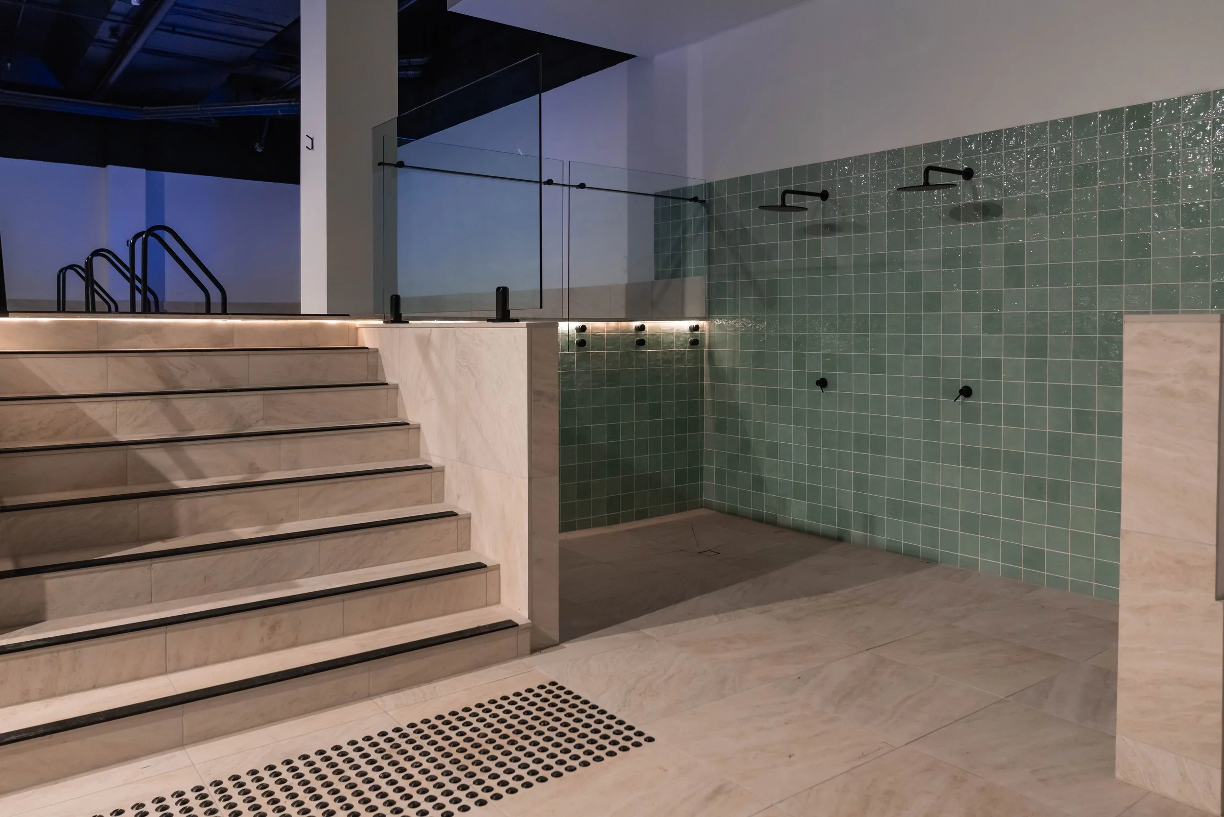 Monsoon shower area in the recovery centre, with  three showerheads, and marble stairs leading up to a pool or spa area.