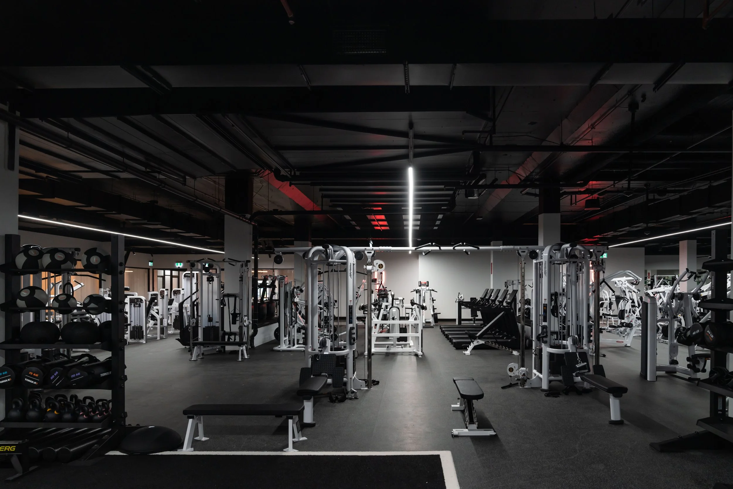 modern gym with various weight machines, free weights, and cardio equipment in dimly lit setting.