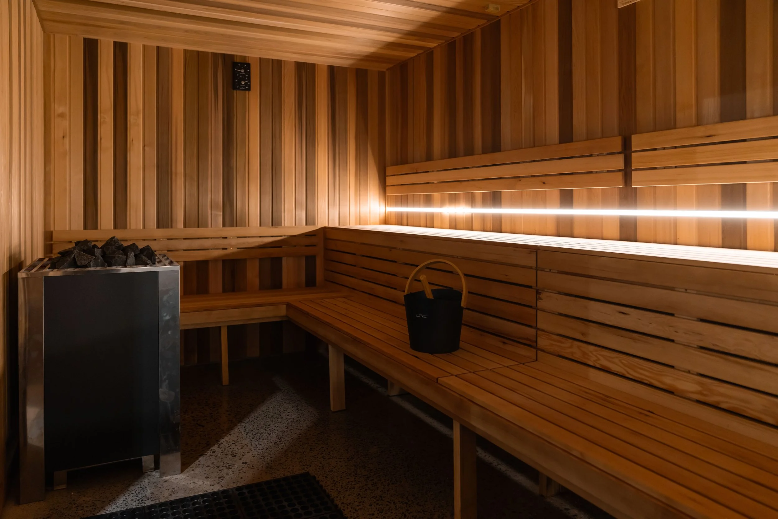traditional rock sauna with bench seating, a heater with stones, and a bucket with a ladle inside.