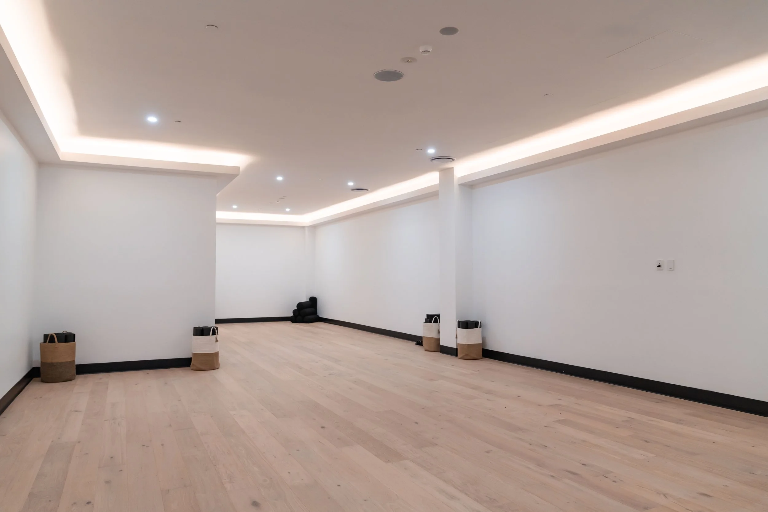 Yoga Studio with white walls, light wooden floor, and recessed ceiling lights. Bolsters and yoga props in the room