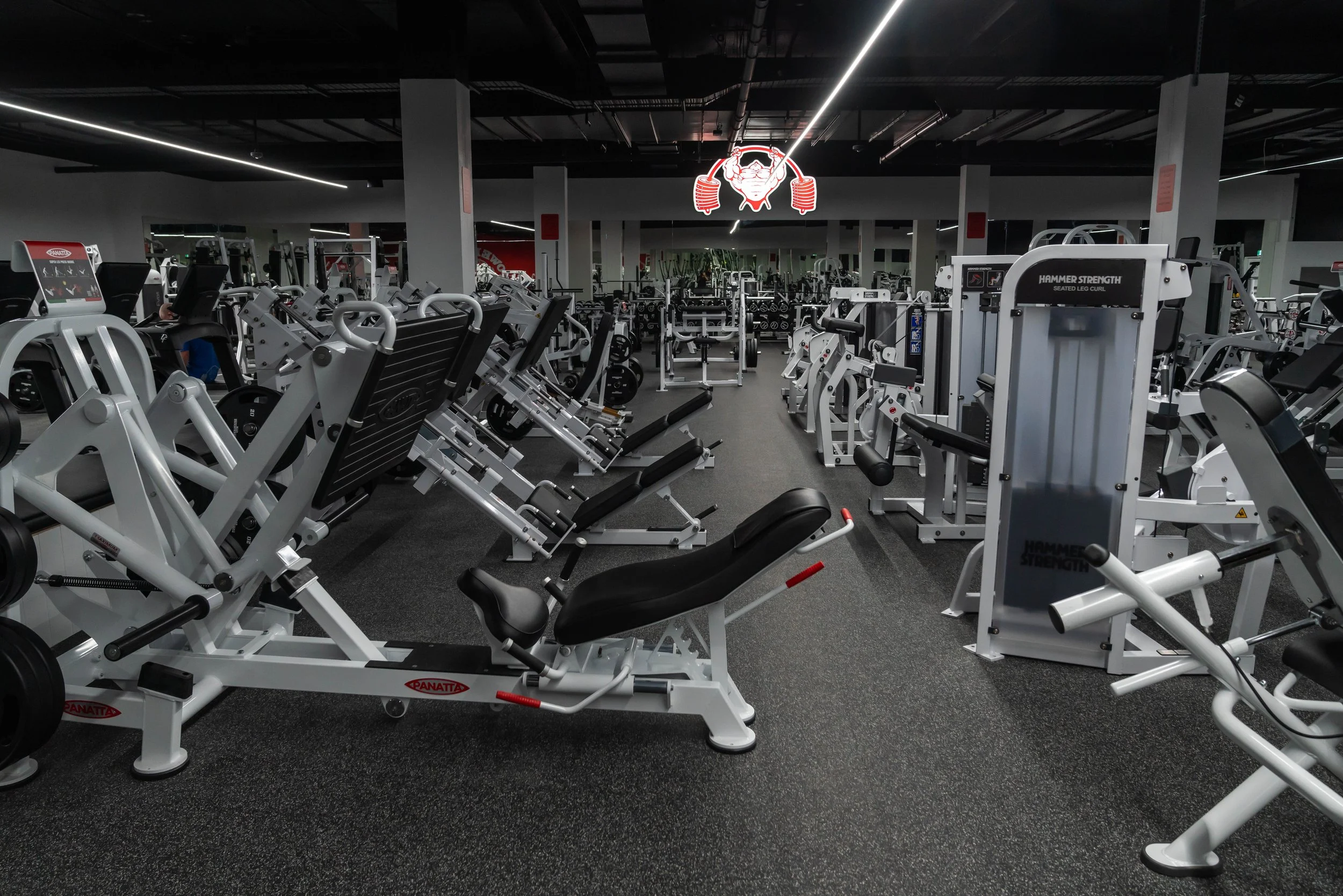 gym with various workout machines, weights, and exercise equipment, with a neon sign of a weightlifter on the wall.