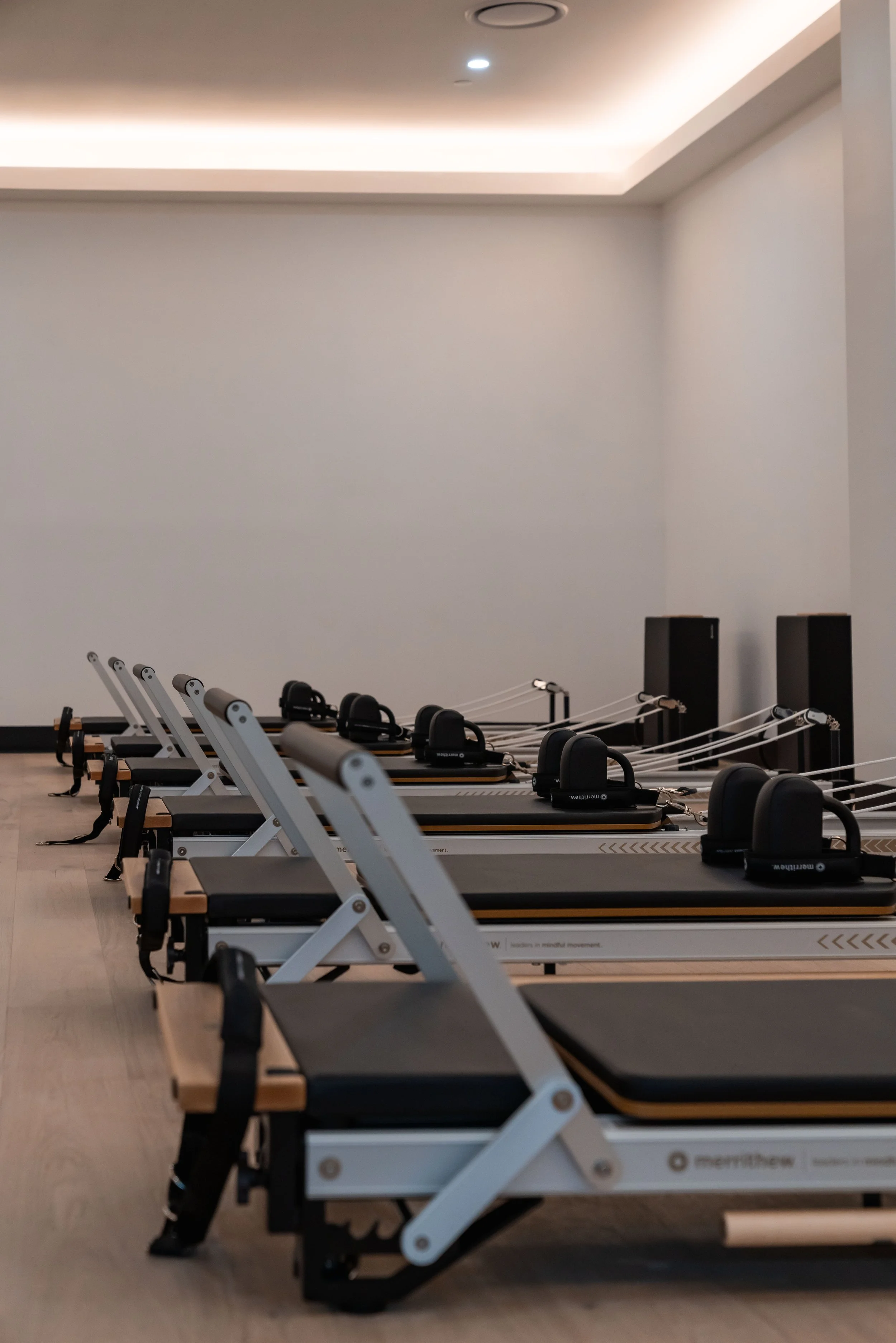 Row of Pilates reformer machines in a modern fitness studio with wooden floors and white walls.