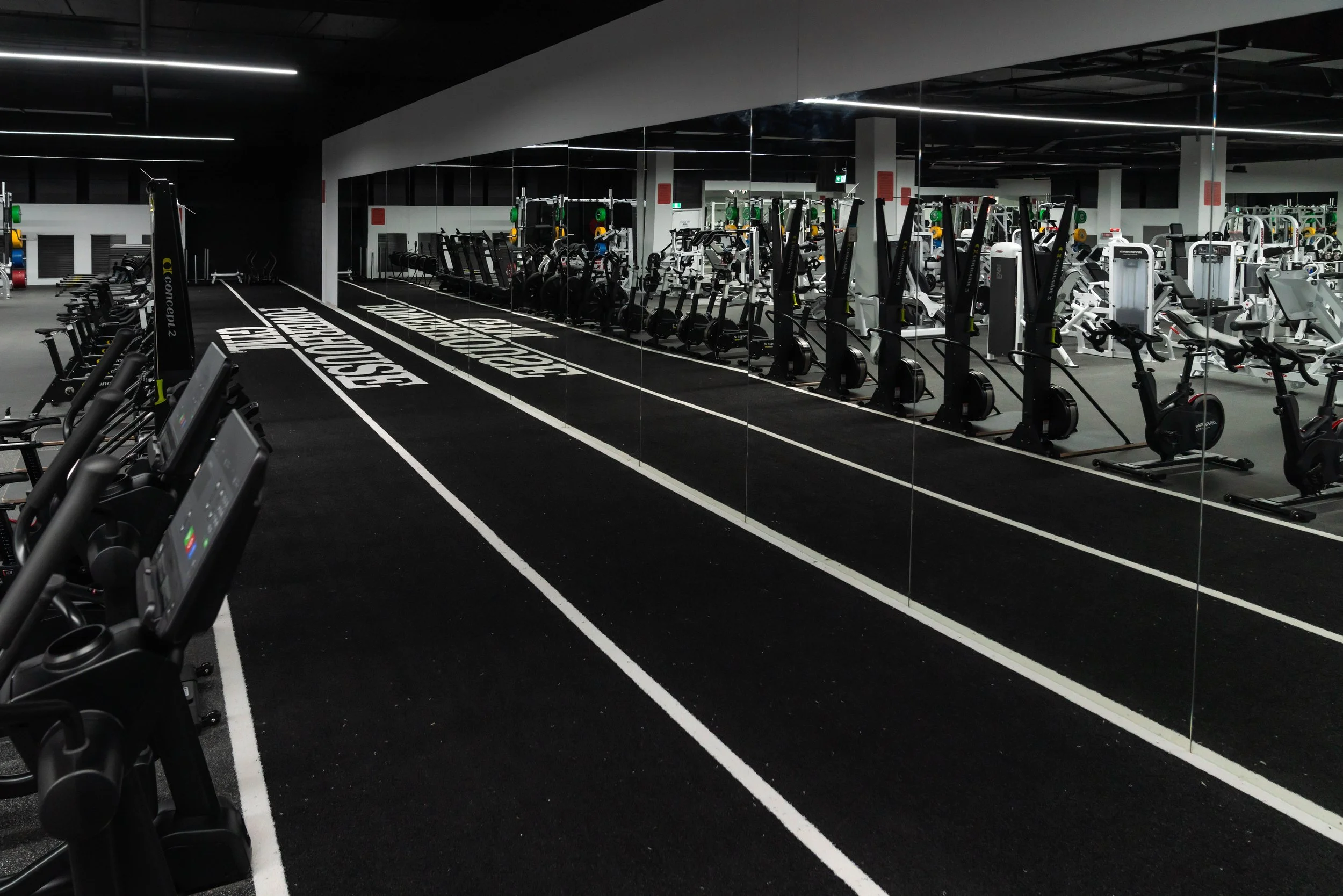 Interior of a modern gym with cardio machines, strength equipment, and a running track with lanes marked as 'CrossFit' and 'Speed.' mirrored wall reflects gym equipment.