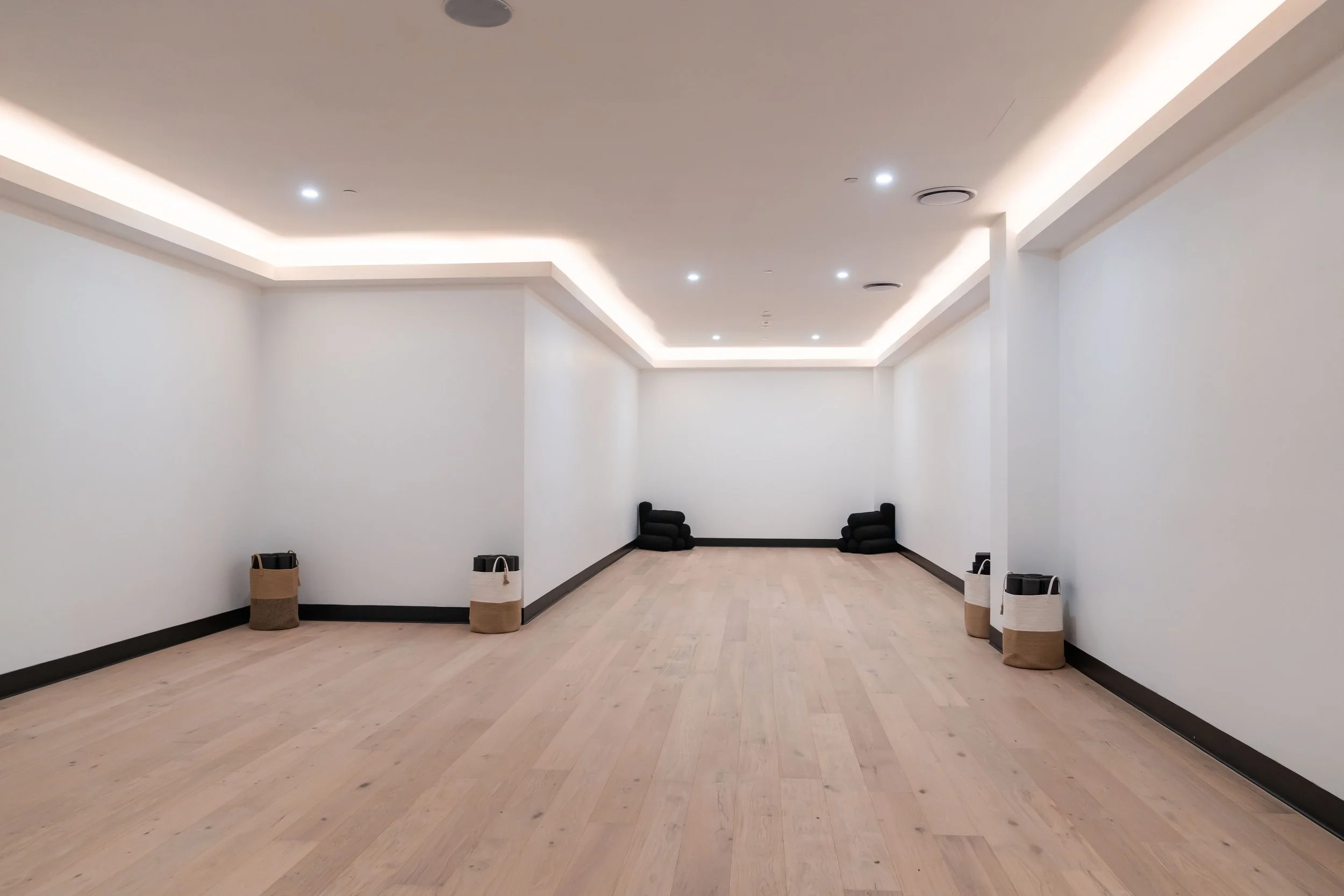 Yoga Studio with white walls, light wood flooring, recessed ceiling lighting, and black yoga mats and other yoga props.
