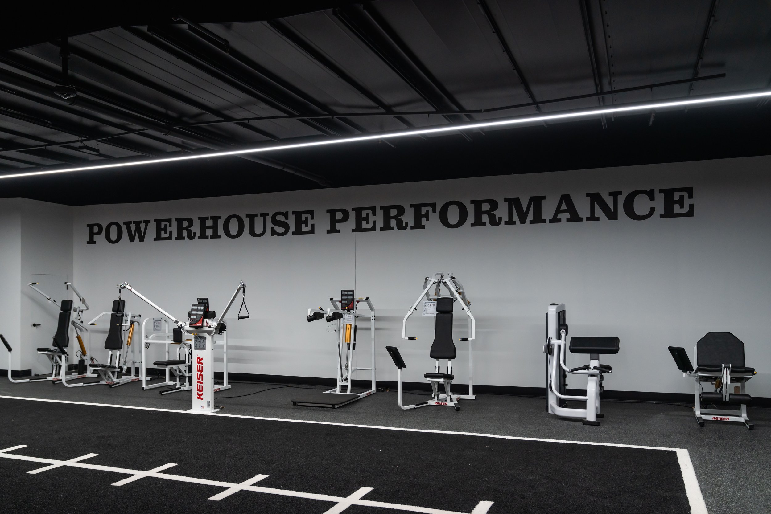Gym equipment in a workout area with a wall sign reading 'Powerhouse Performance.'