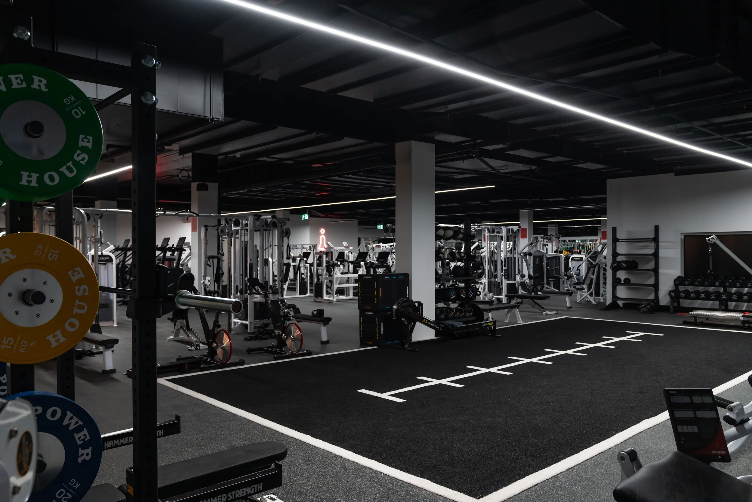 modern gym with weightlifting equipment, cardio machines, and a black floor marked with white lines for functional training.