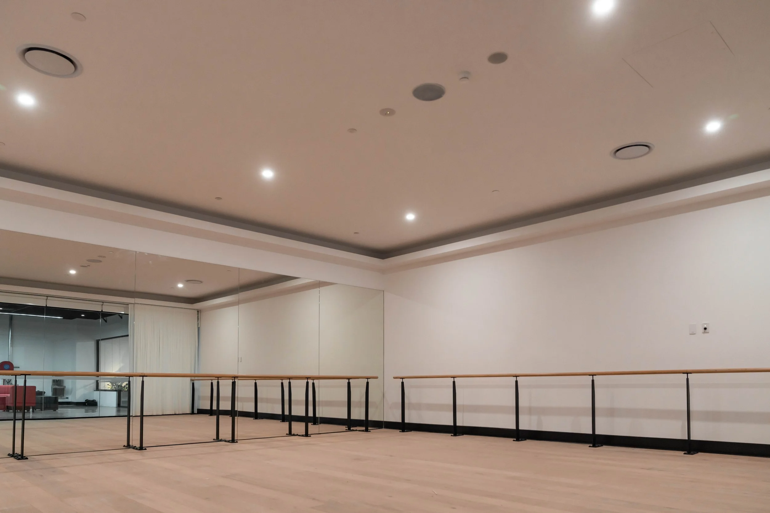 Barre studio with wooden floors, ballet barres, a large mirror on the wall, and ceiling lights.