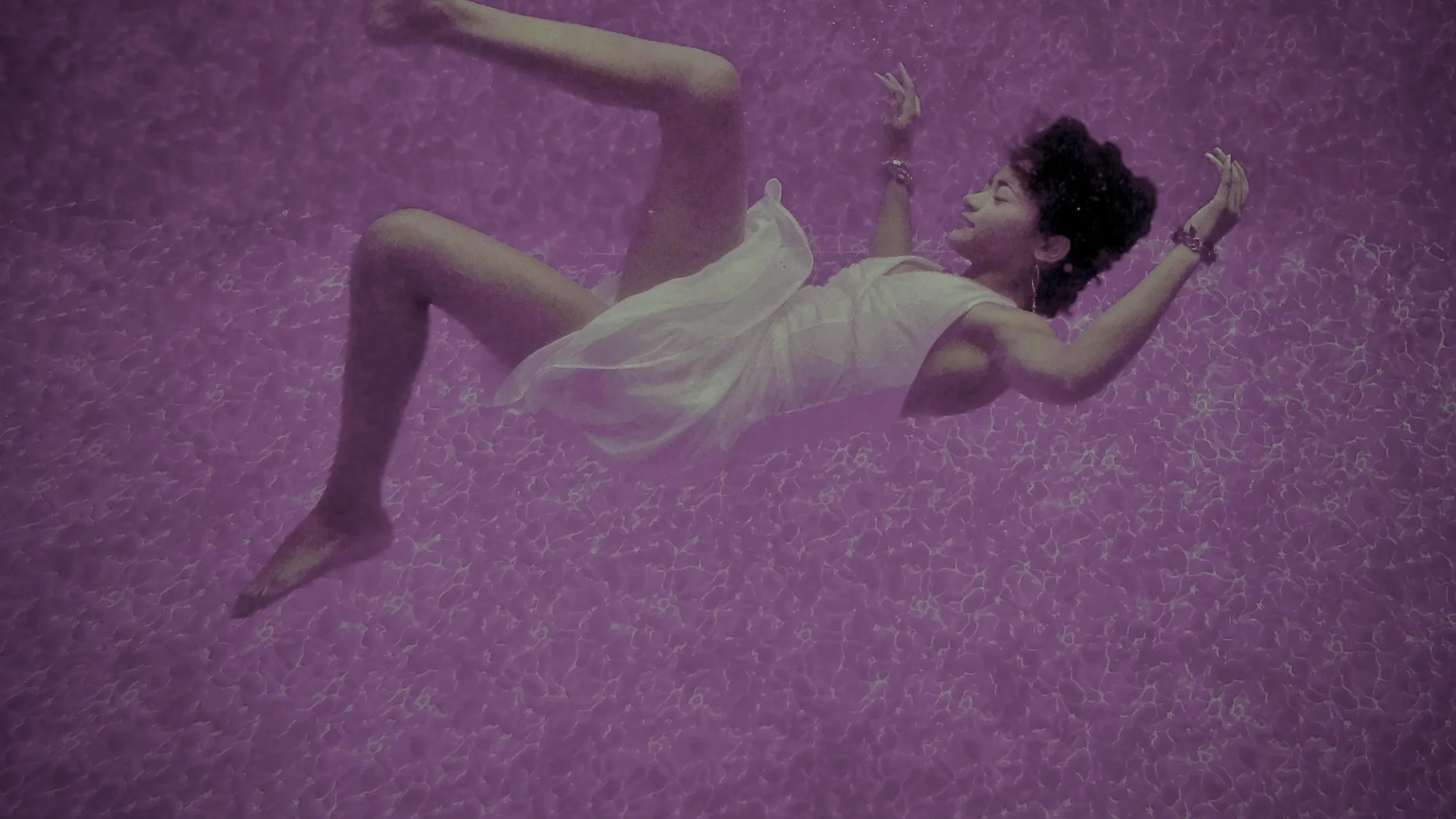 Woman in a white dress floating underwater against a purple textured background.