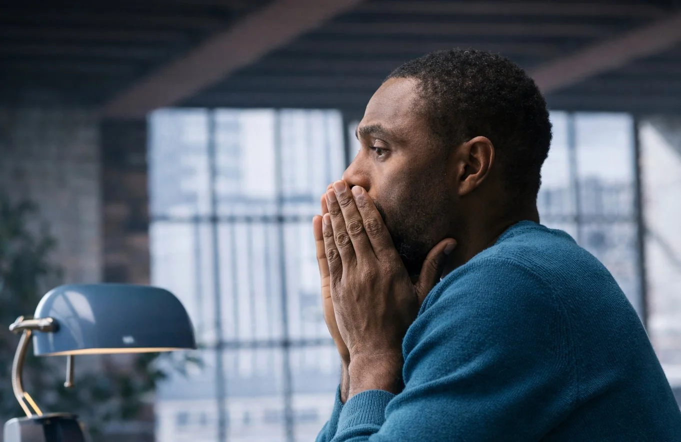 Man sitting by a window with his hands near his face
