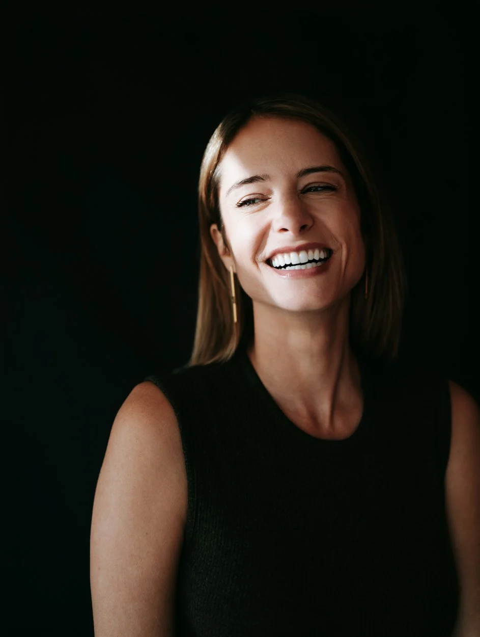 woman with black backdrop smiling in the shadow of the sun