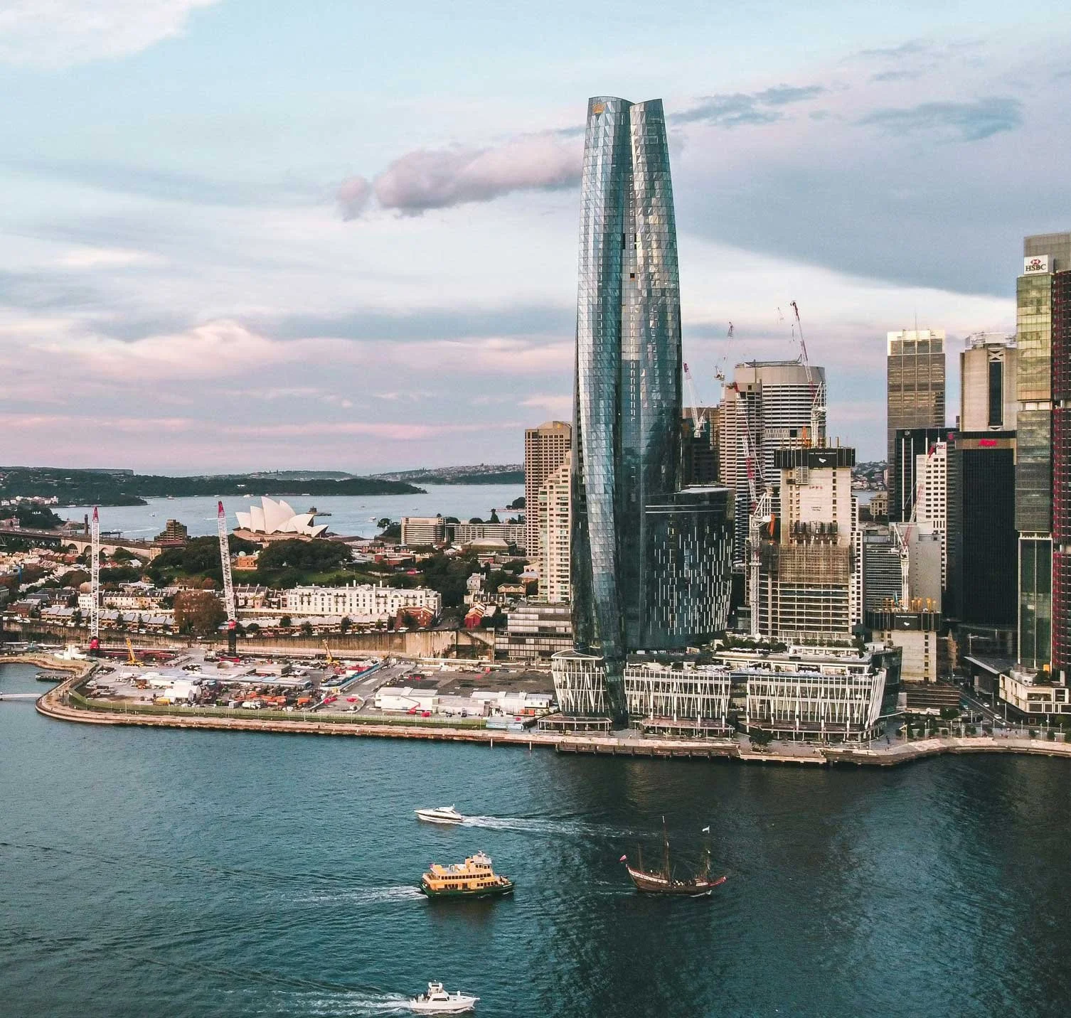 Sydney city skyline featuring a tall buildings next to a body of water with boats.