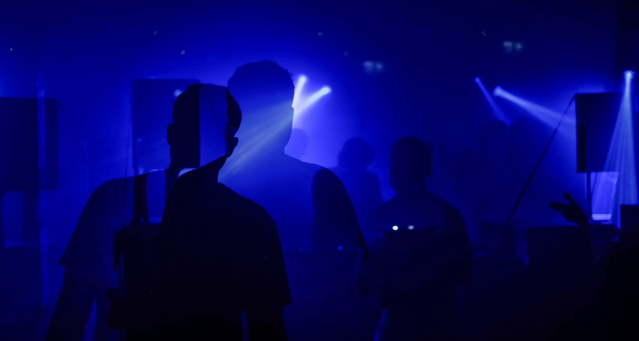People dancing at a dark nightclub with blue lights and fog