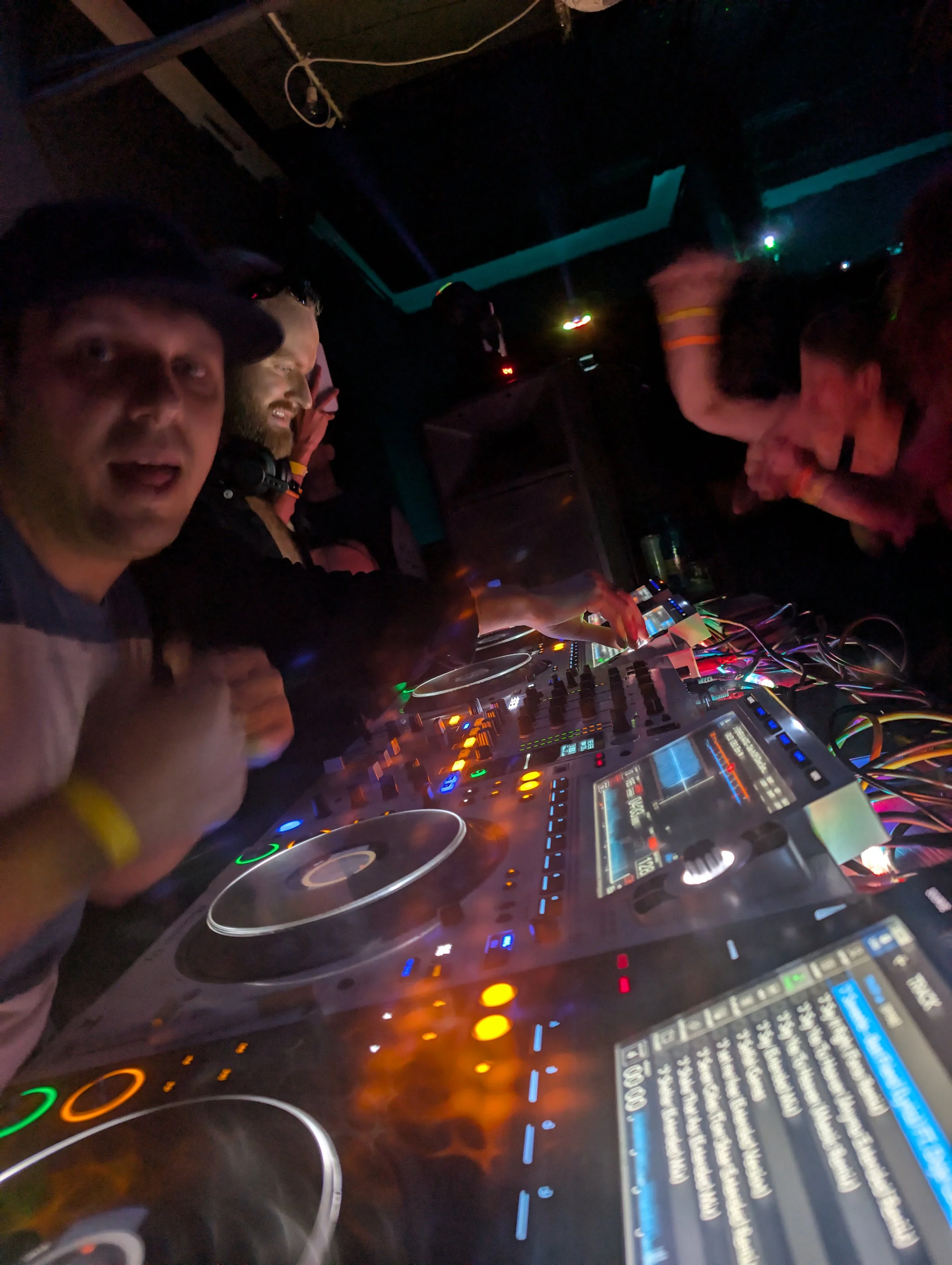 People DJing at a nightclub with DJ equipment, colorful lights, and a dark background.