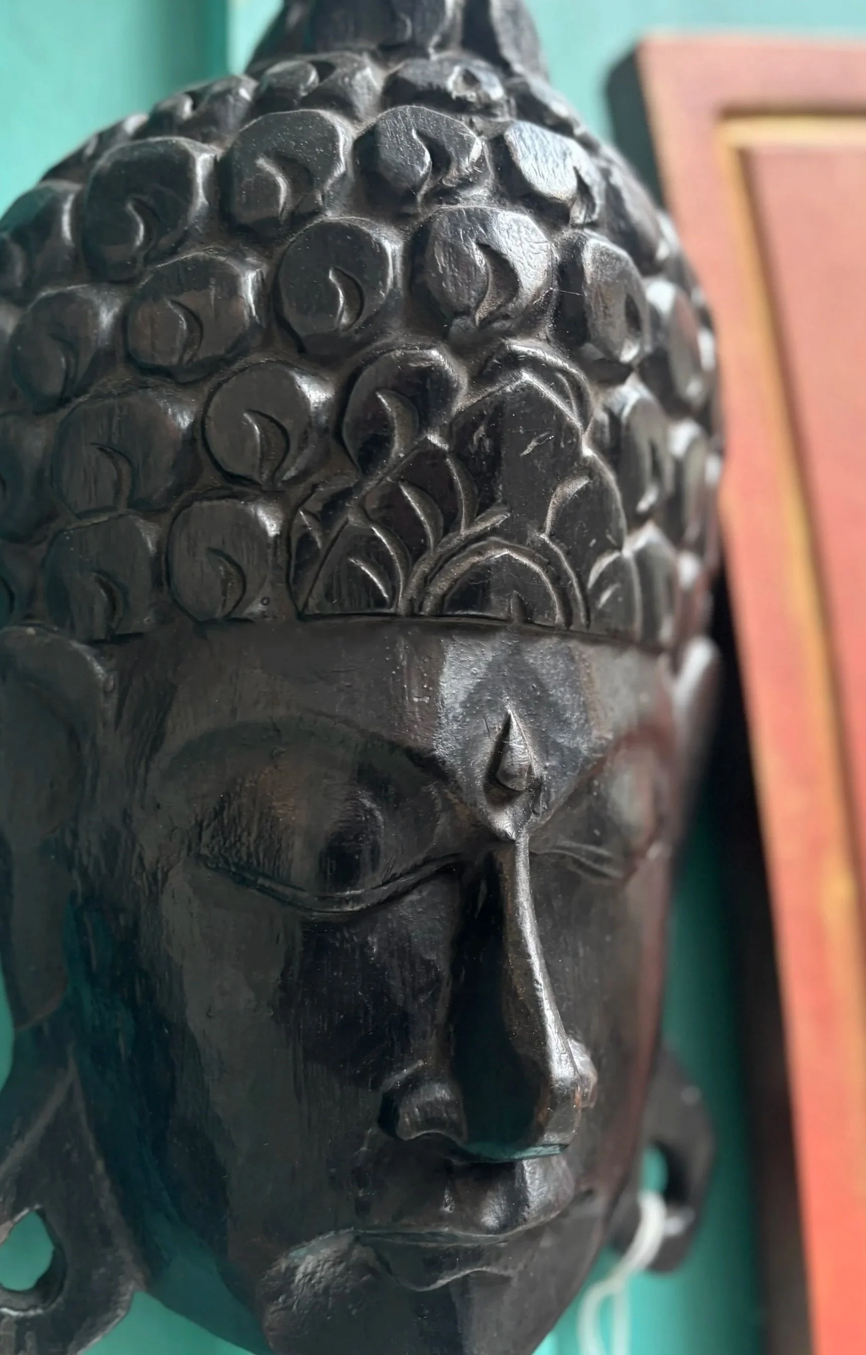 Close-up of a black Buddha face sculpture made of wood or ceramic, showing detailed features and a serene expression.