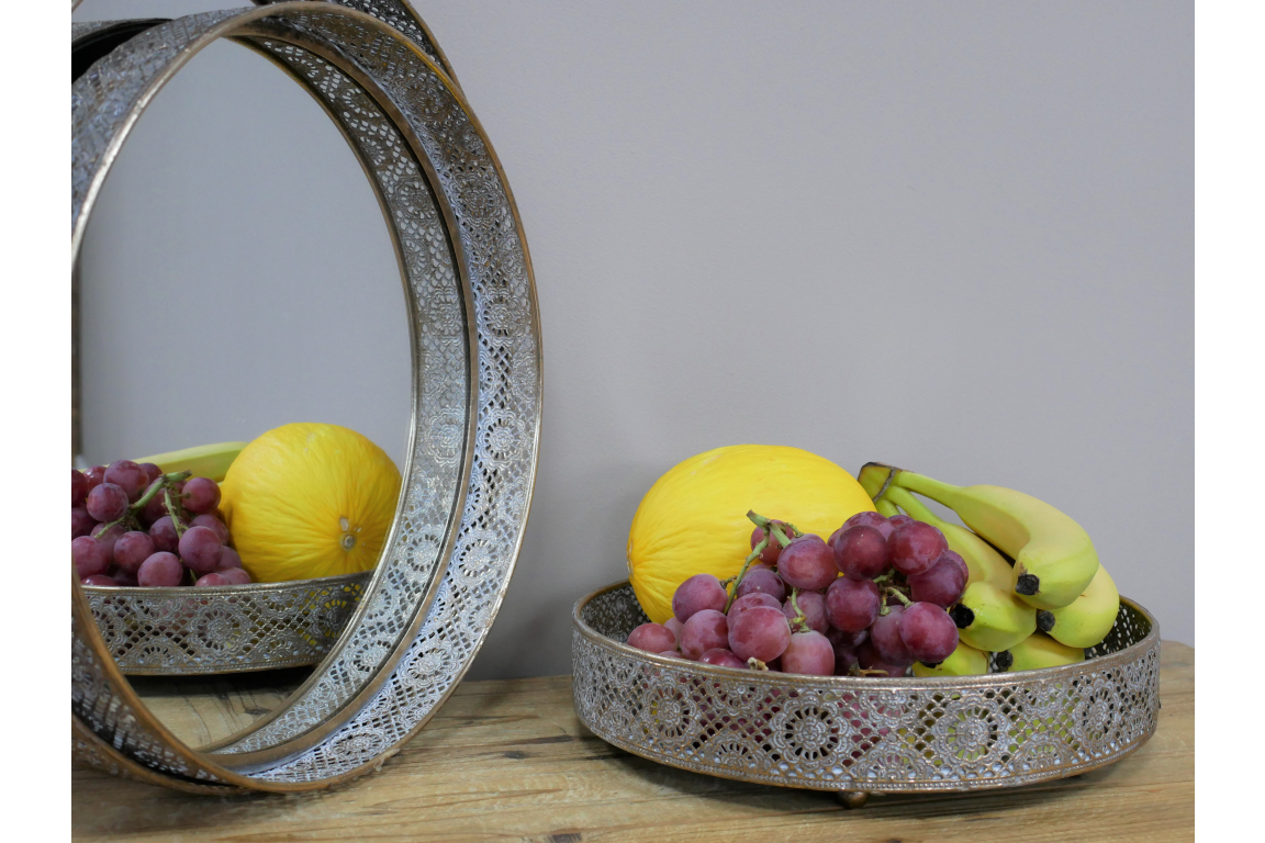 Tray with yellow melons, purple grapes, and bananas, with a decorative silver mirror reflecting part of the tray and fruits.