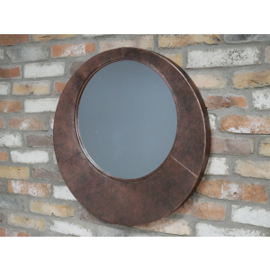 Round mirror with a brown frame hanging on a brick wall.