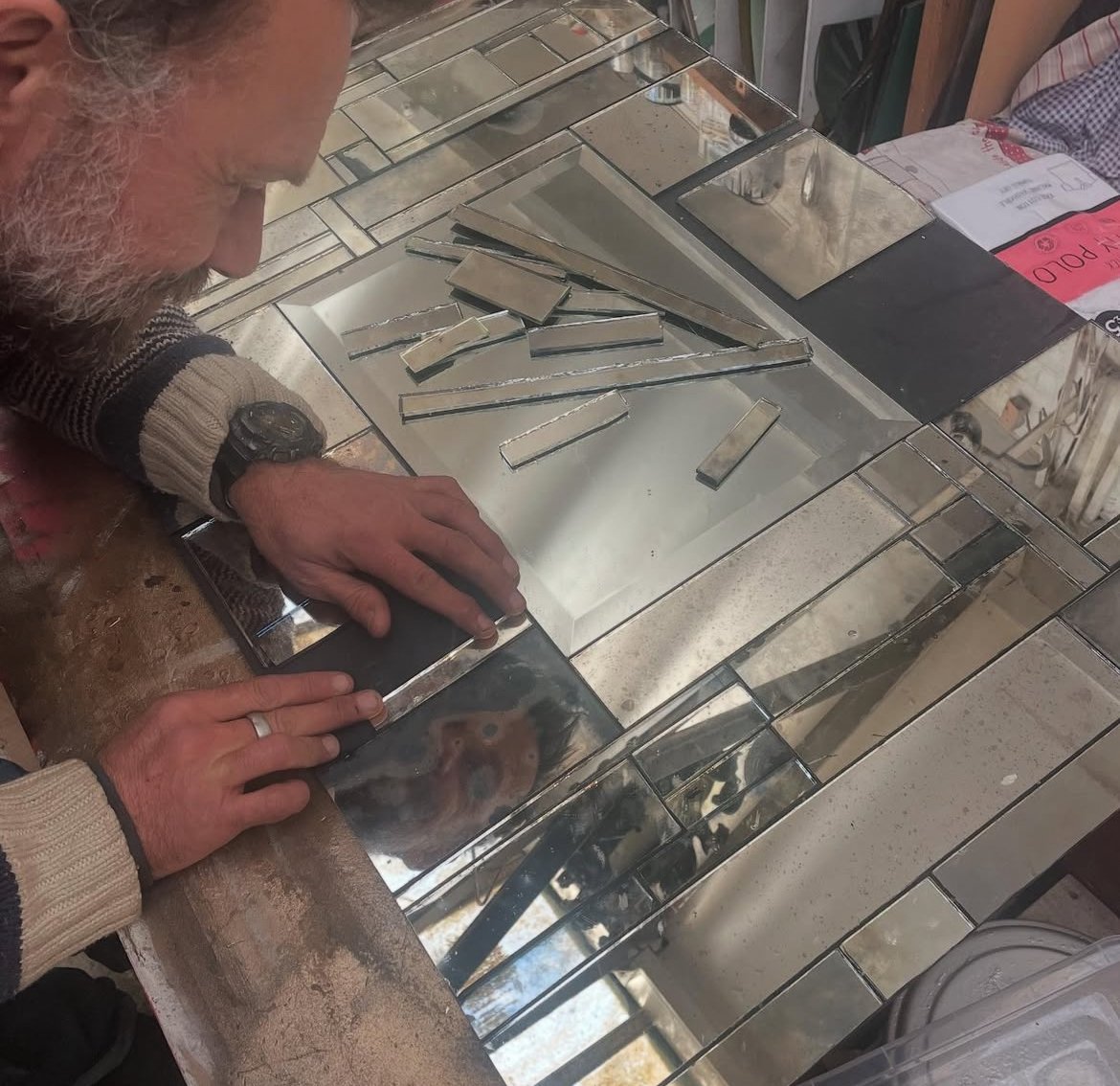 A man working with cut and assembled mirror pieces on a tiled counter.