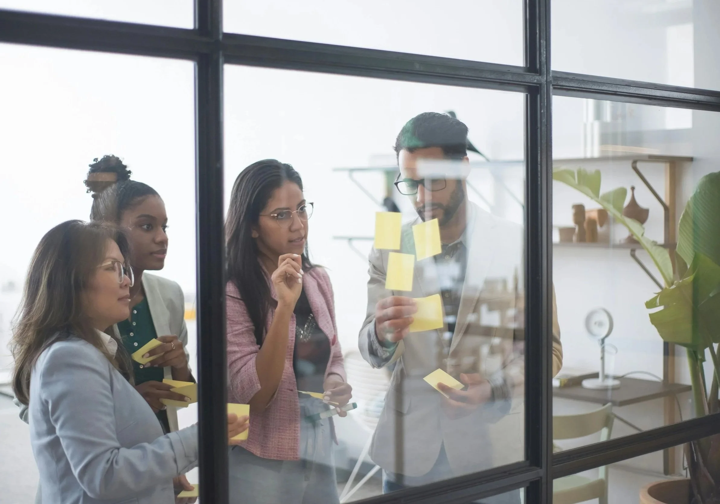 Leaders collaborating with sticky notes on a glass wall during a team workshop