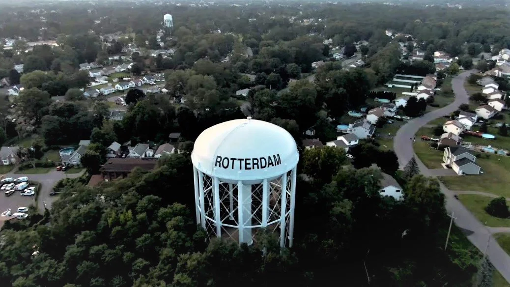 A water tower labeled 'Rotterdam' surrounded by trees and a residential neighborhood with houses and winding roads.