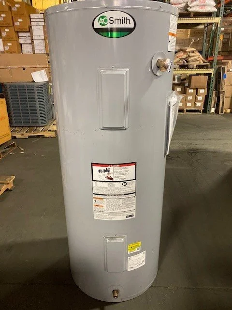 A gray A.O. Smith water heater standing in a warehouse with shelves filled with boxes and items.