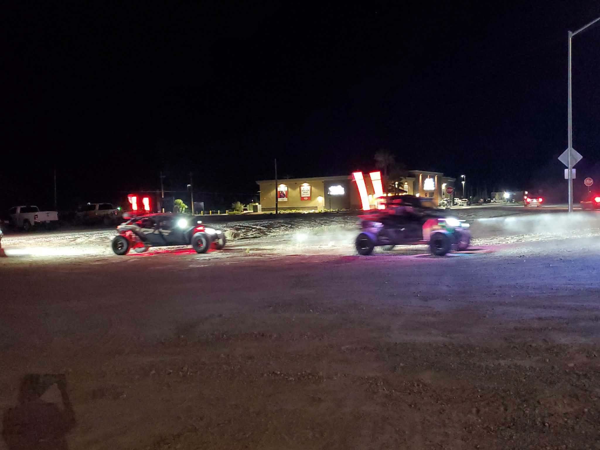 Off-road UTVs with colorful light bars kicking up dust on a night ride at the September 2026 Nye County SxS monthly meet