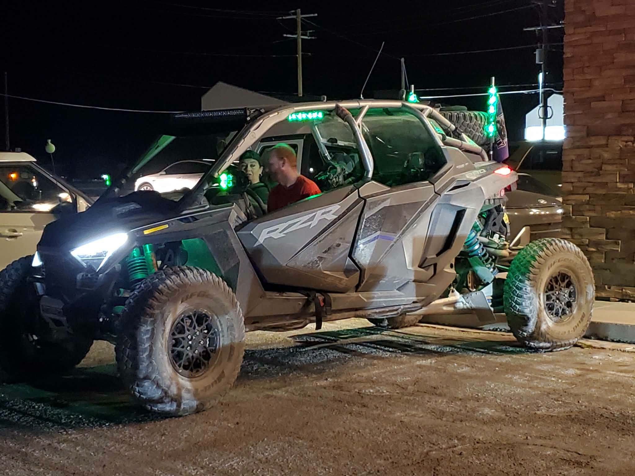 Riders in a Polaris RZR lit up with green interior lighting at night during the September 2026 Nye County SxS monthly meet