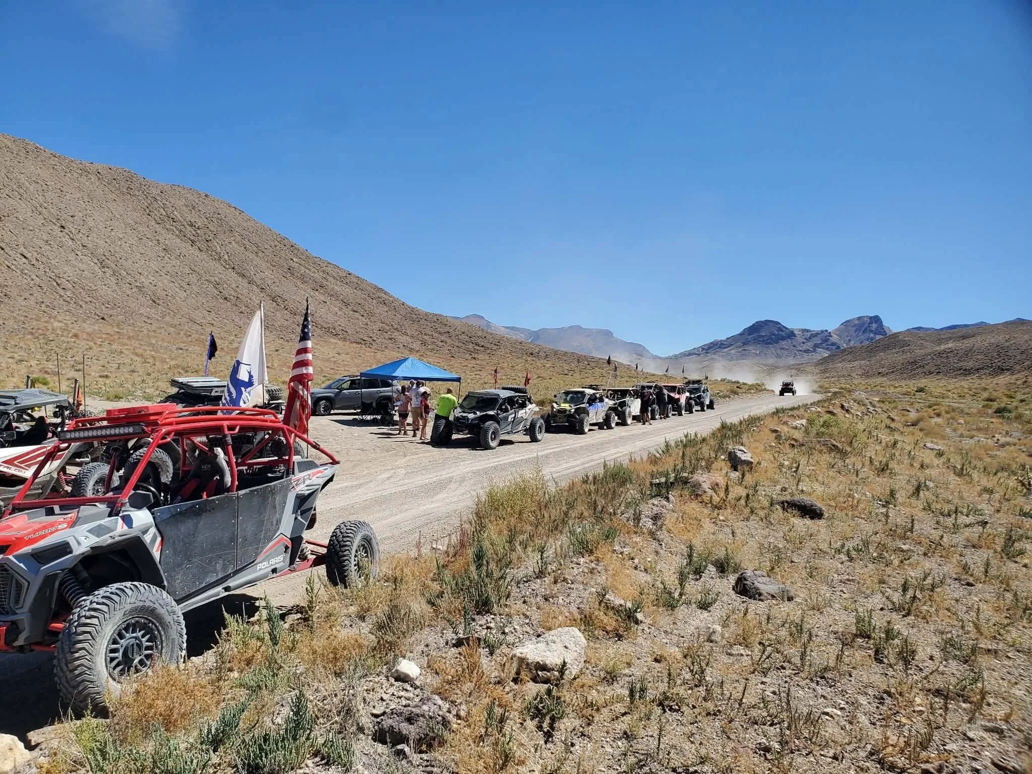 Line of off-road UTVs with an American flag staged and heading out onto the desert trail at the 2026 Dyer - Fish Lake Poker Run