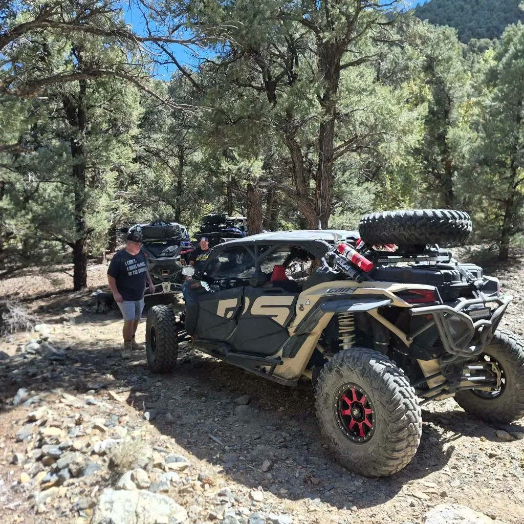 Custom olive-colored off-road UTV with red rims parked on a rocky forest trail during the 2026 Dyer - Fish Lake Poker Run